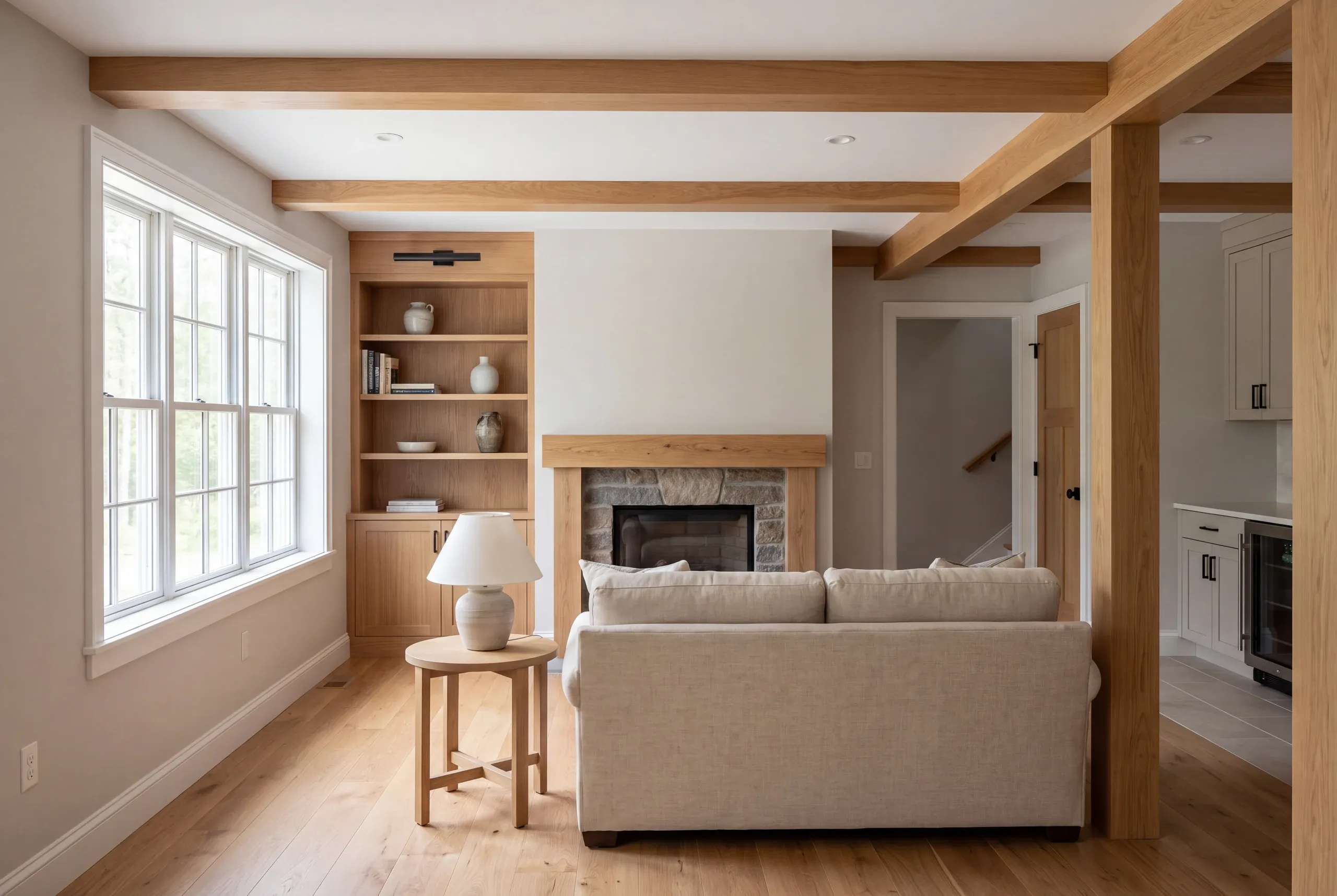 Interior view of a completed lower-level recreation room featuring exposed wooden ceiling beams, a stone fireplace, built-in shelving, hardwood flooring, and a beige sofa.