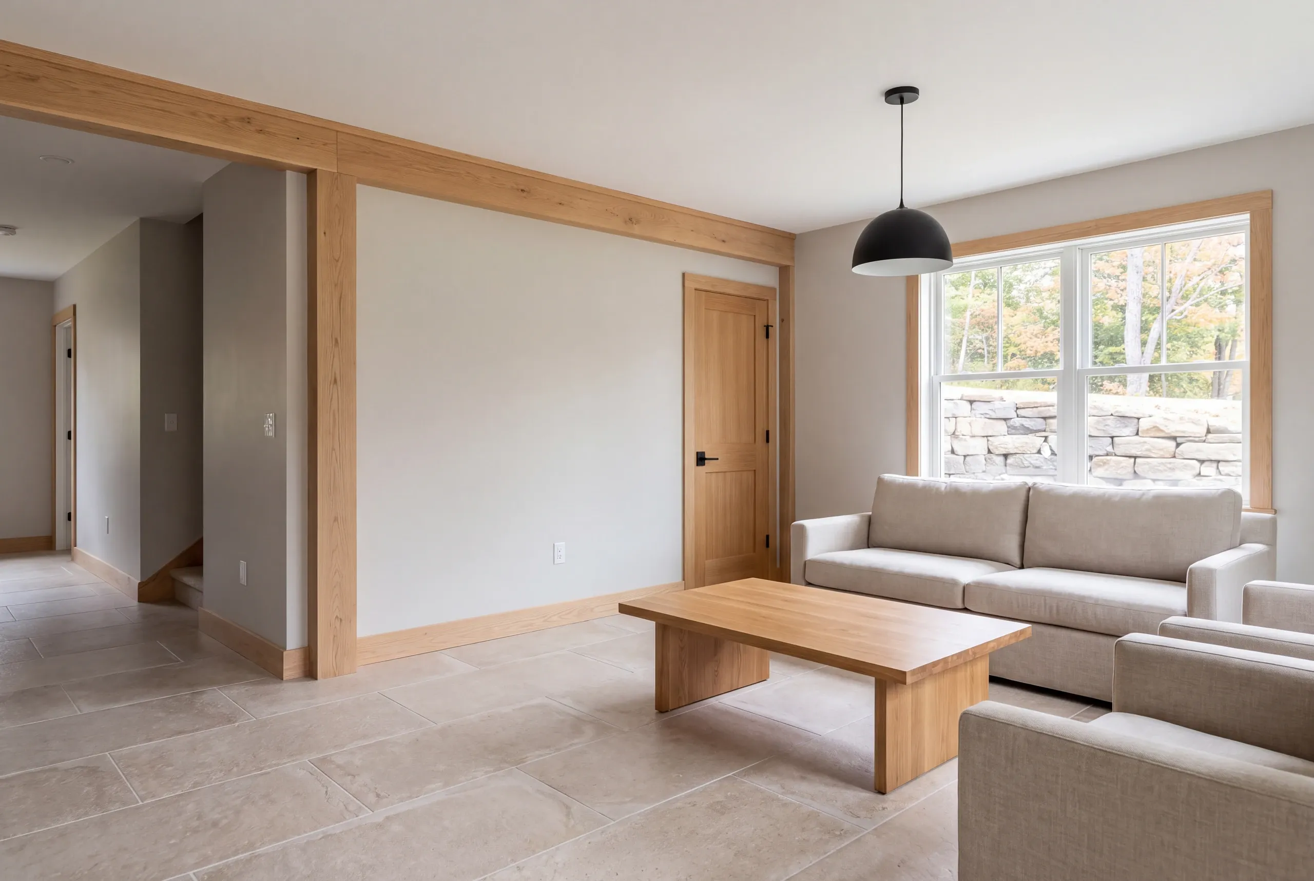 A finished room with tile floors, a wooden coffee table, a light-colored sofa and armchairs, a window looking outside, and a modern black pendant light hanging from the ceiling.