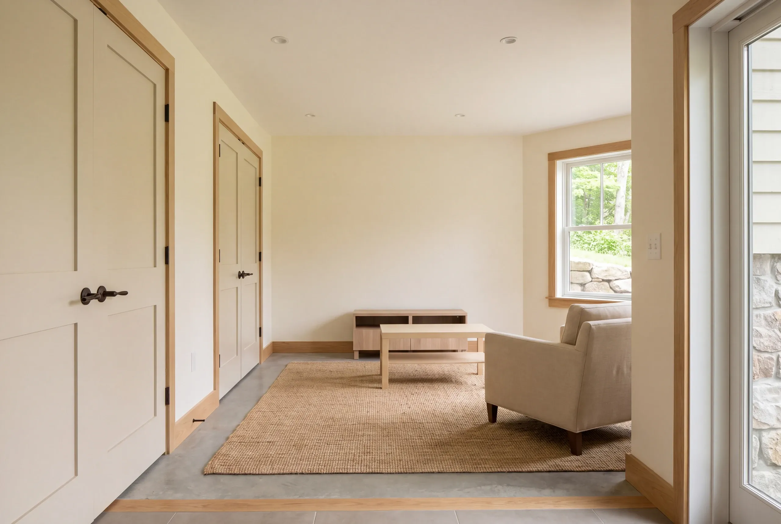 A finished room with cream-colored walls, light wood trim, a concrete floor with a rug, an armchair, and several closed doors.