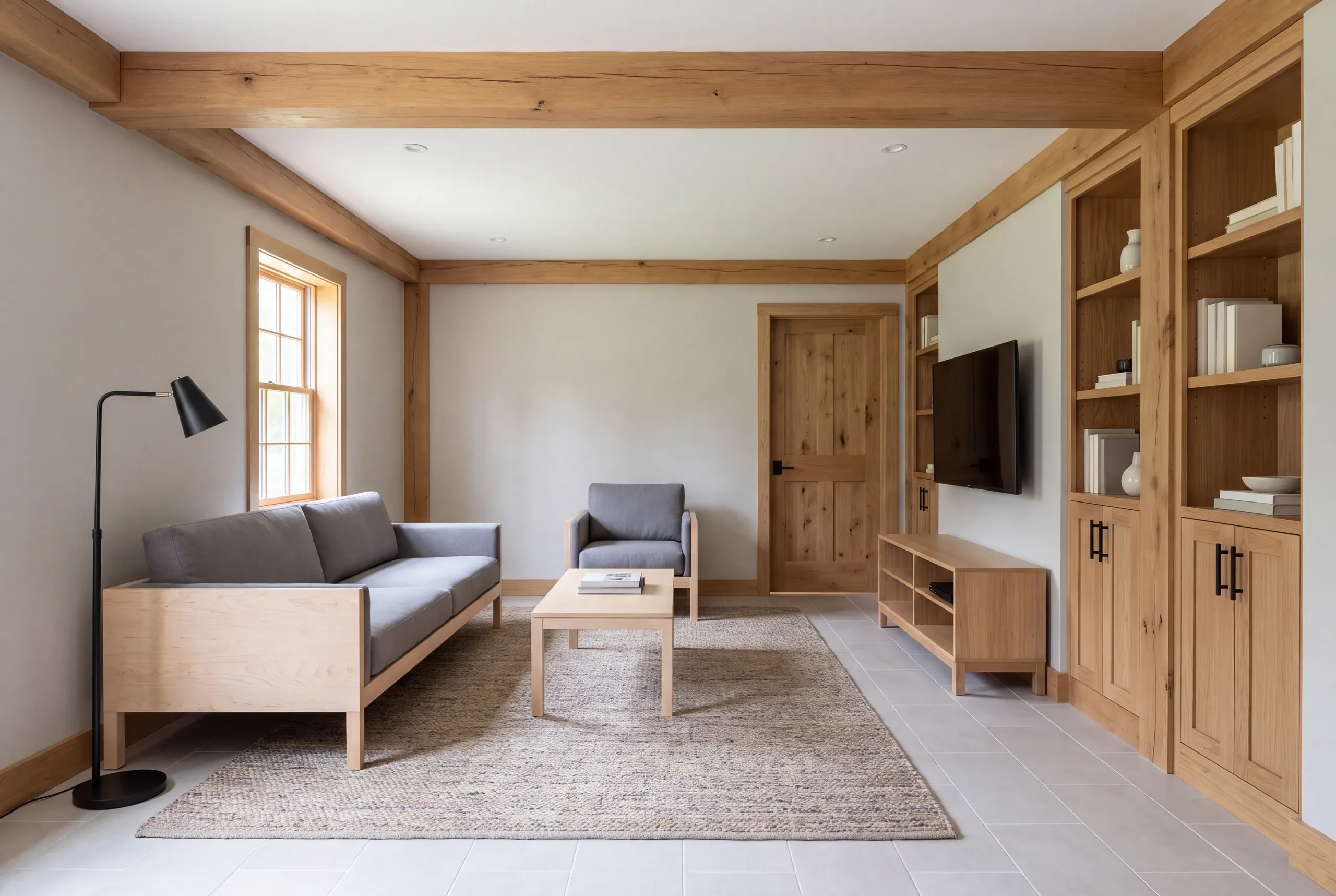 A finished recreation room featuring a grey sofa, armchair, wooden coffee table, built-in bookshelves, and a television on the wall.