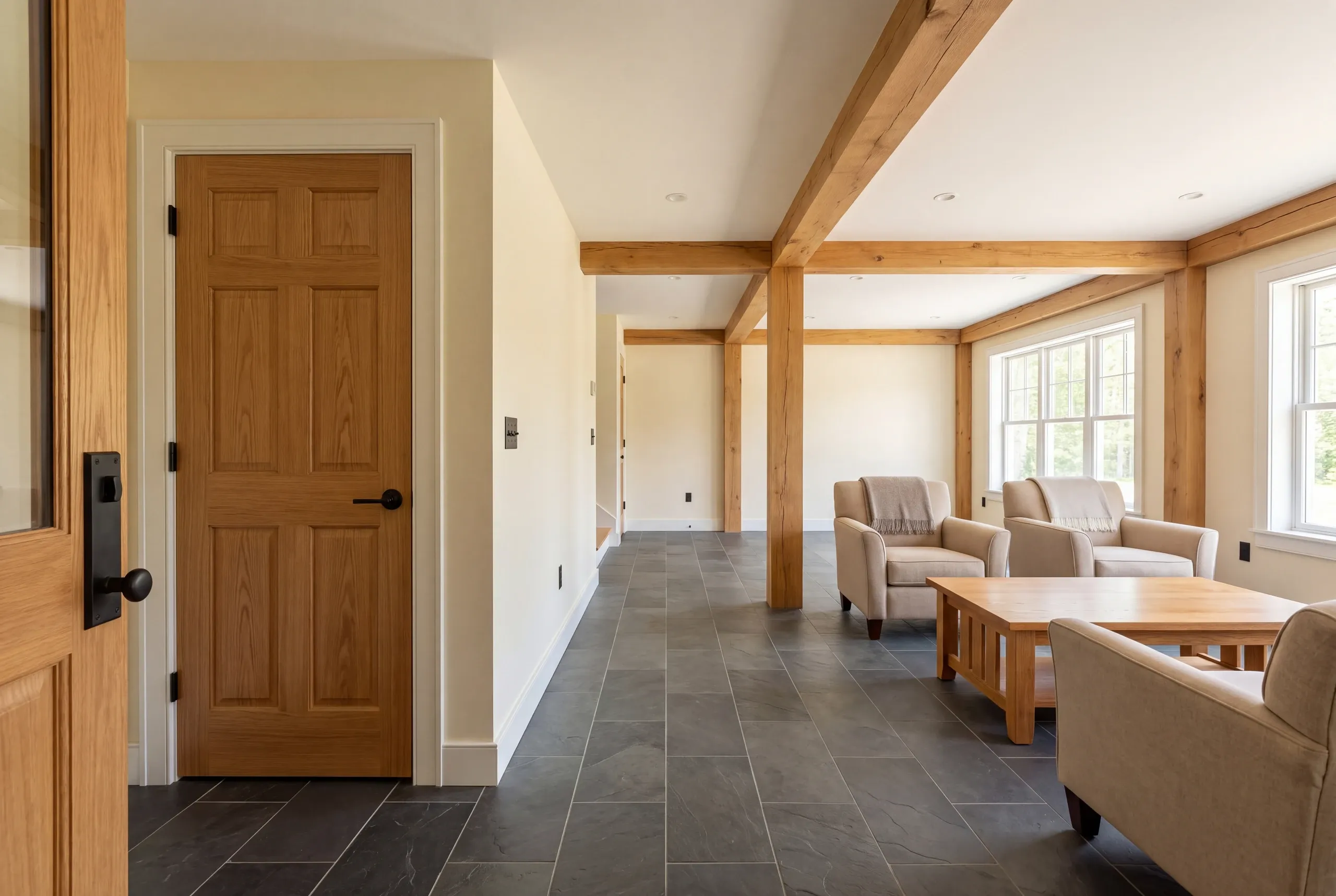 Interior view of a finished room featuring a wooden door, tiled flooring, exposed wooden beams, and armchairs with a coffee table.