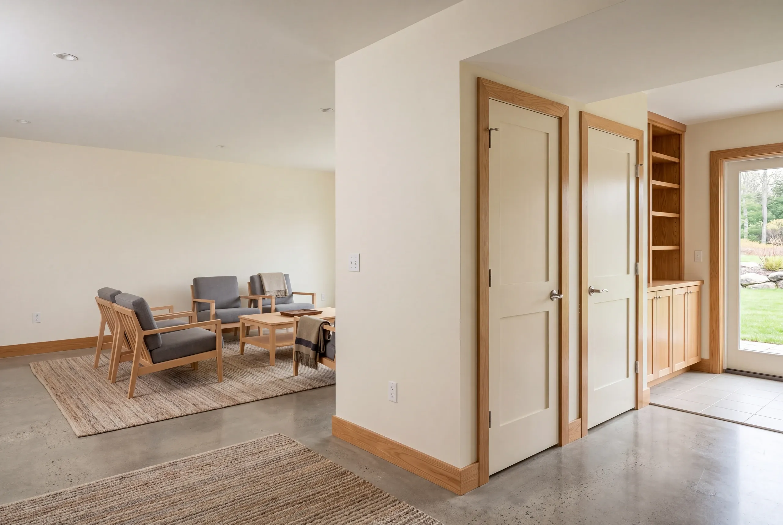 Interior view showing a finished room with wooden armchairs, closed doors, built-in shelving, and a glass exterior door.