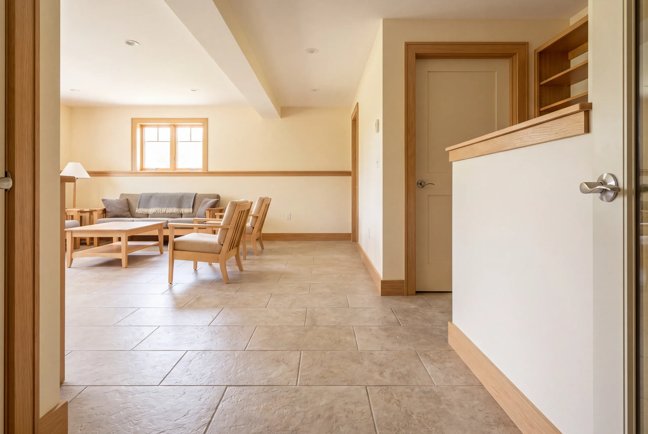 A finished basement room with tile flooring, a sofa, chairs, and a closed door.