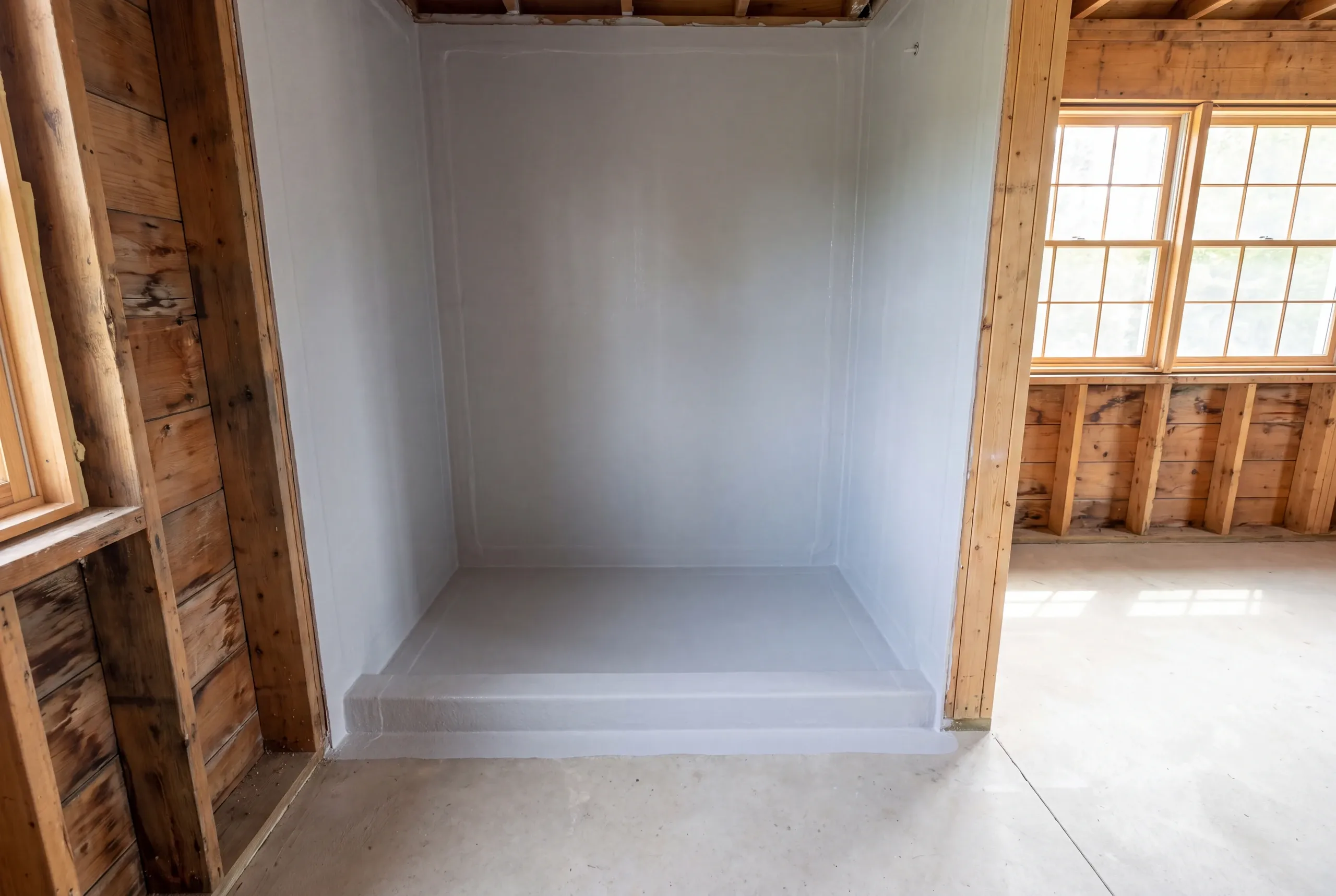 An empty shower alcove with a continuous grey waterproofing membrane applied to the walls, floor, and curb.
