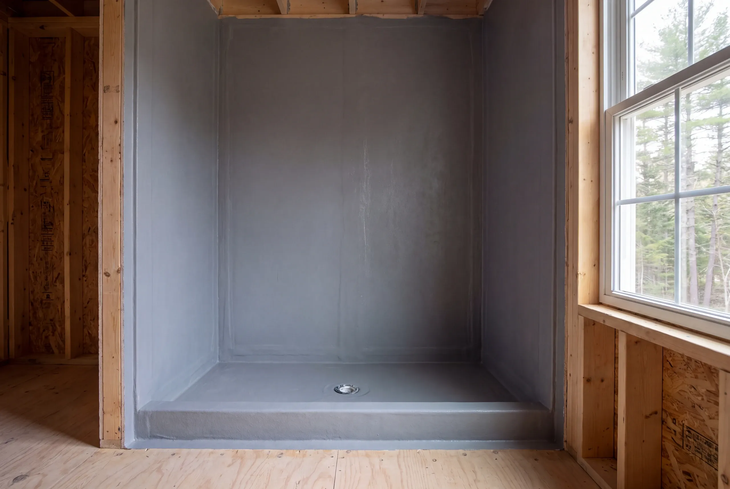 An unfinished wooden framed alcove with walls and floor coated in a continuous gray waterproofing membrane.