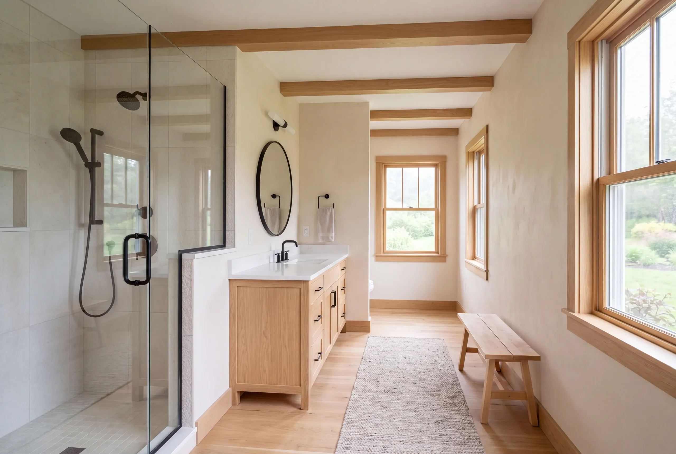 A bright remodeled bathroom features a glass-enclosed shower, a wooden vanity with a round mirror, and wooden ceiling beams.