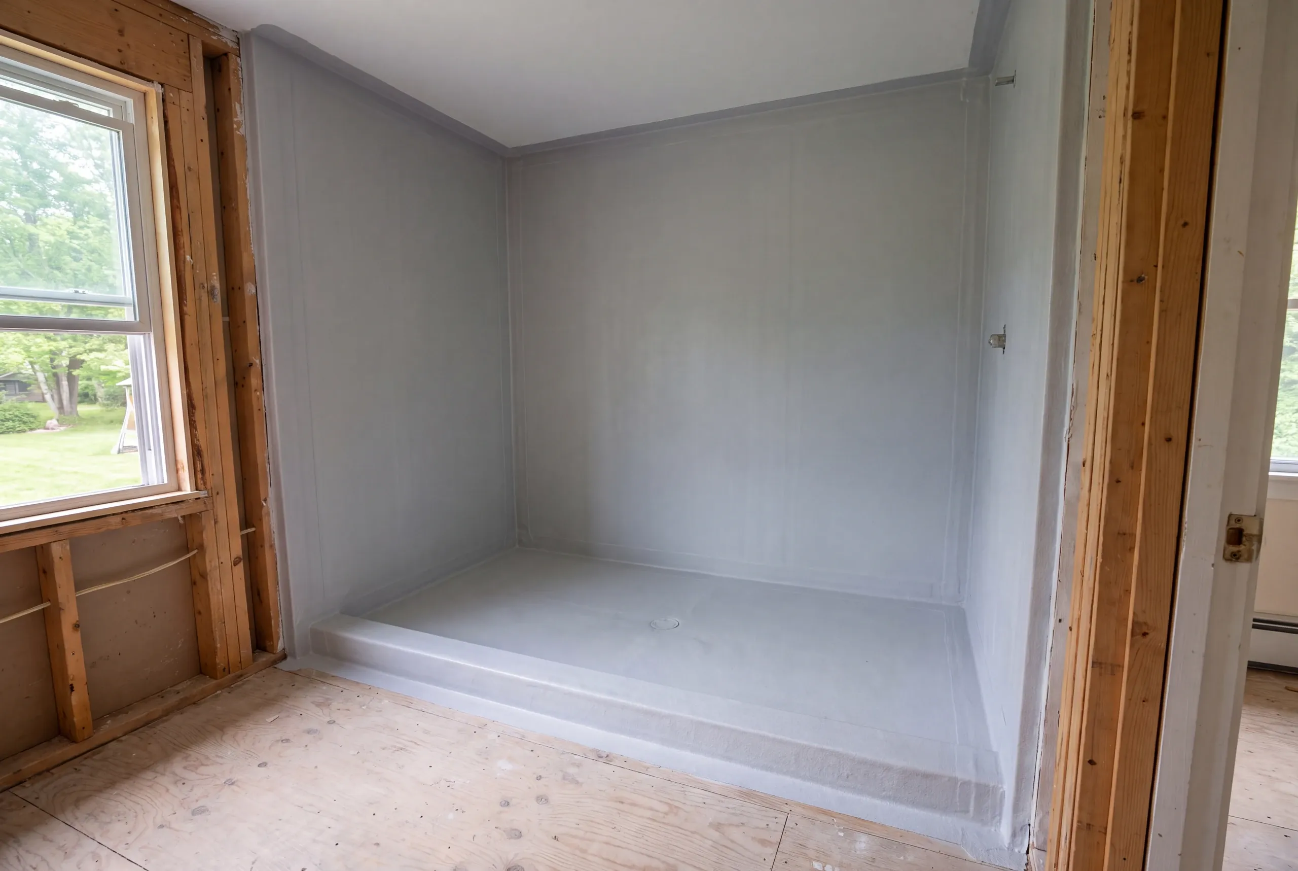 An empty shower alcove coated with a gray continuous waterproofing membrane before tile installation.