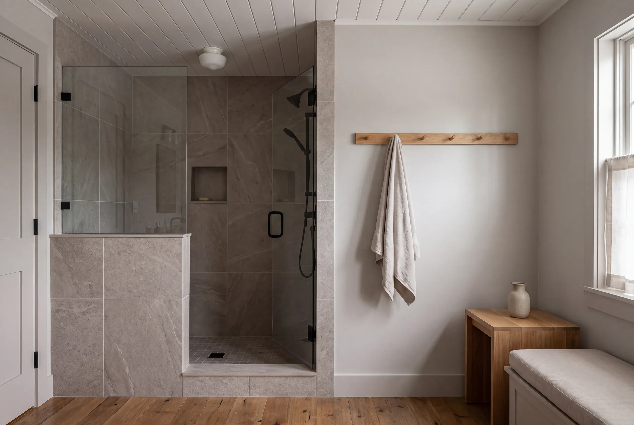 A finished tiled shower enclosure with glass doors sits beside a wall with a wooden peg rail and a towel hanging on it.