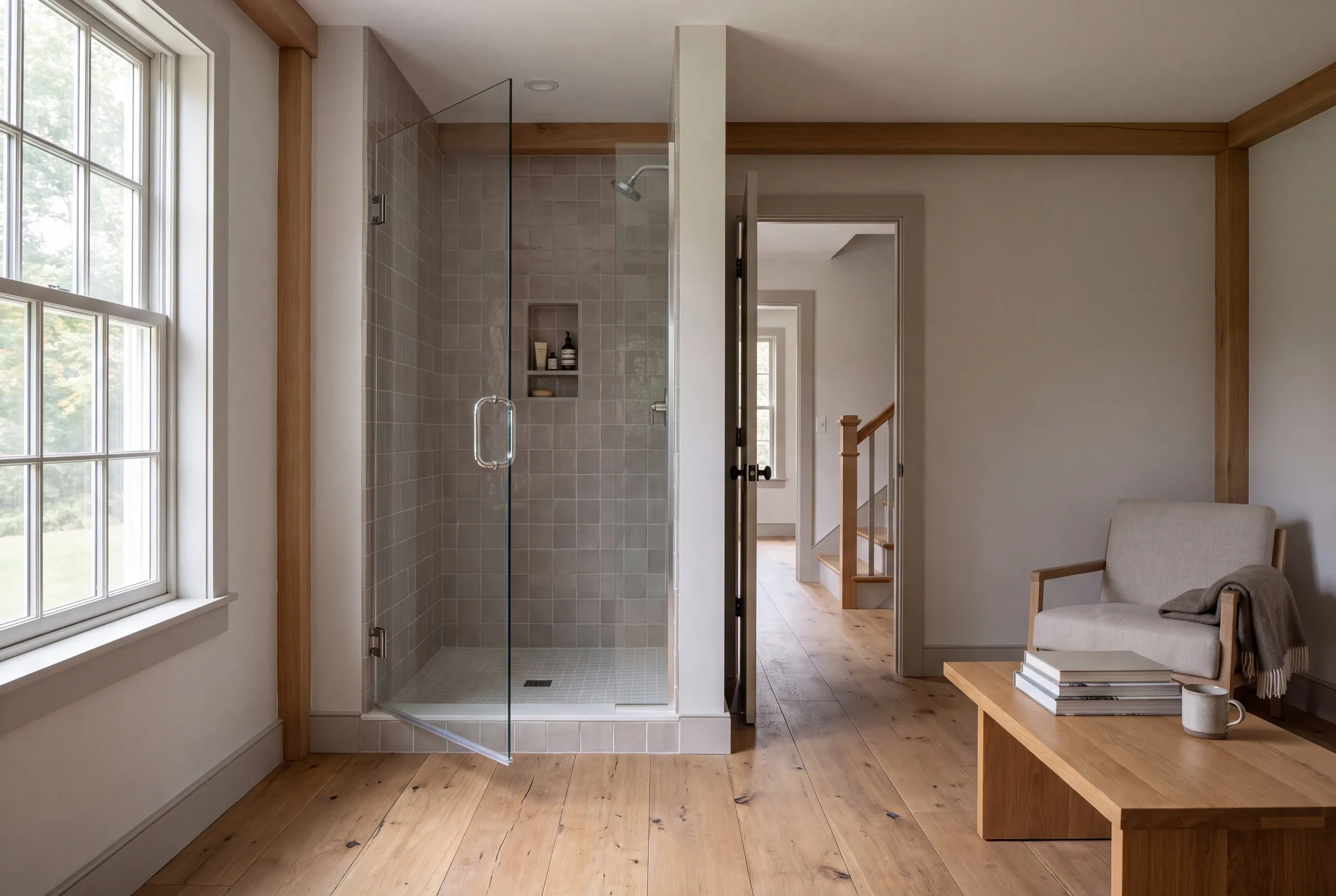 A tiled walk-in shower with a glass door in a finished room with wooden floors and a chair.