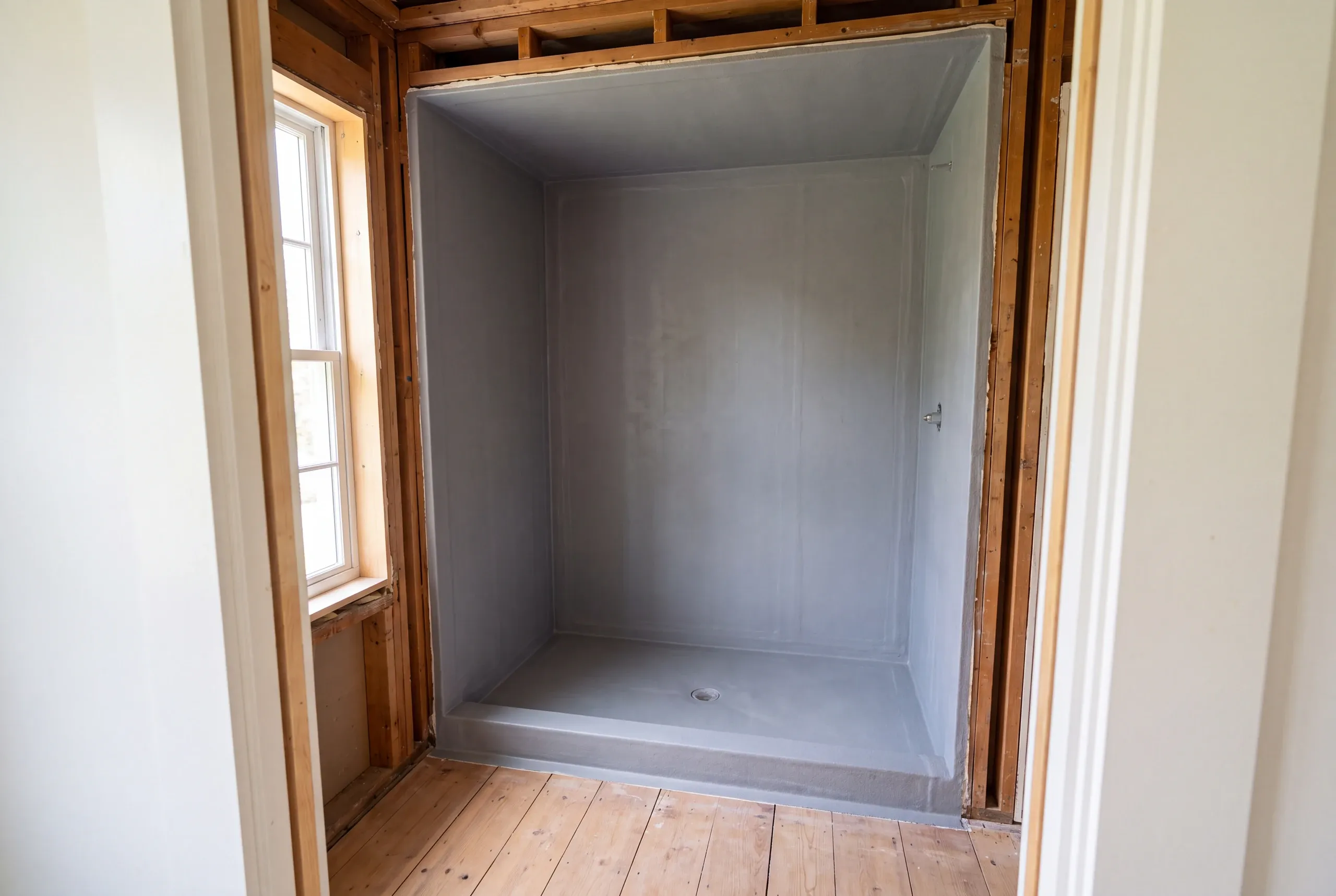 An empty shower alcove with gray waterproofing applied to the walls, curb, and pan before tile installation.