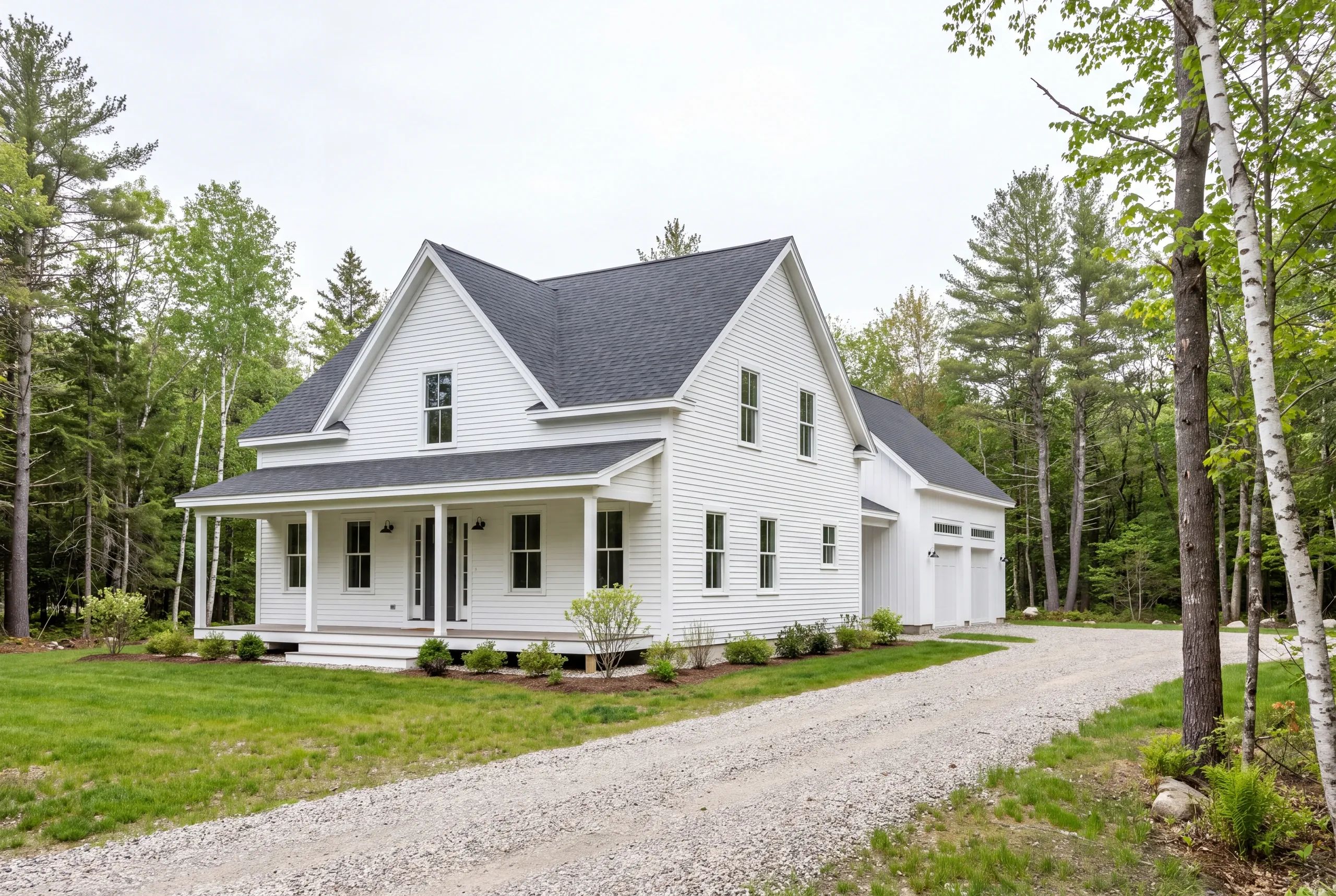 Exterior view of a two-story white house with a covered front porch and a gravel driveway surrounded by trees.