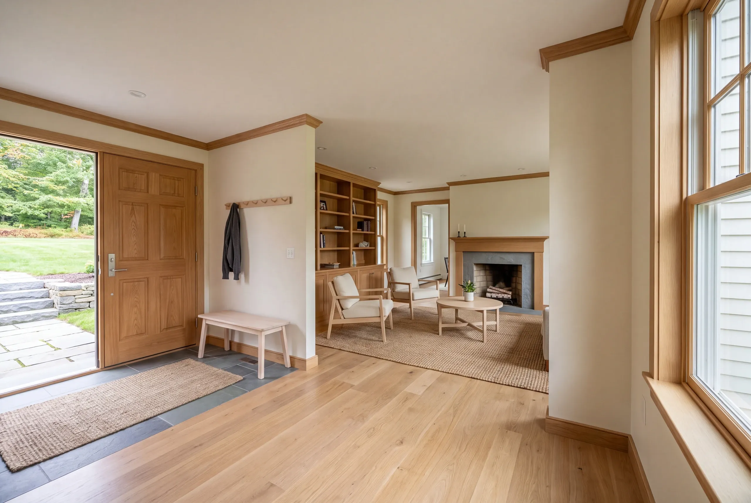 Interior view showing a hardwood entryway with an open wooden front door and a connected living room with a fireplace and armchairs.