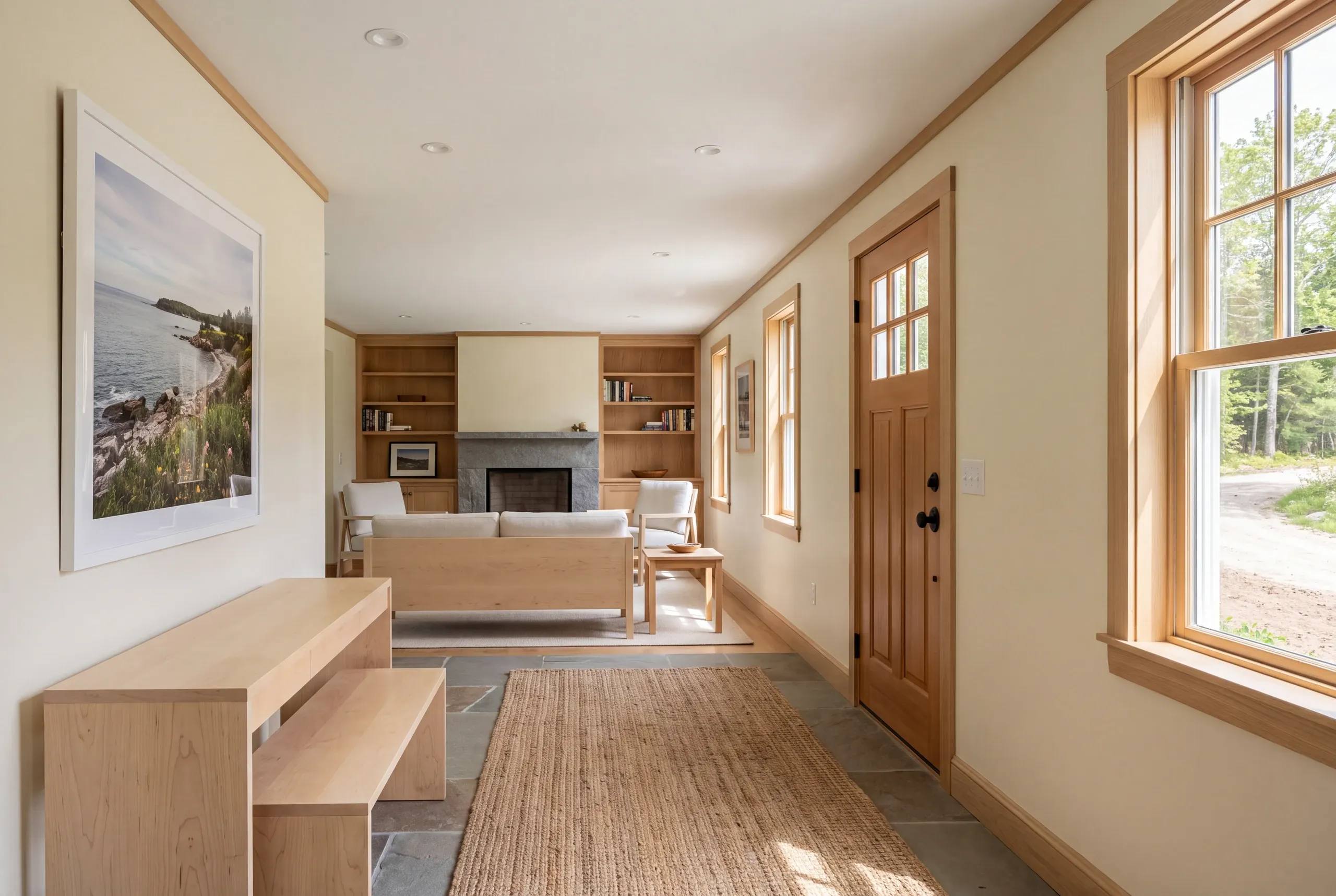 An interior view showing a finished entryway with a wooden bench and console table, leading into a connected living room with a fireplace and built-in shelving.