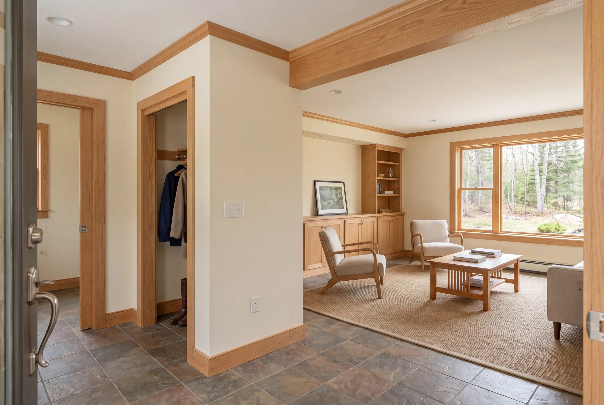 View from an open doorway into an entryway and a connected living room furnished with chairs, a coffee table, and built-in shelving.