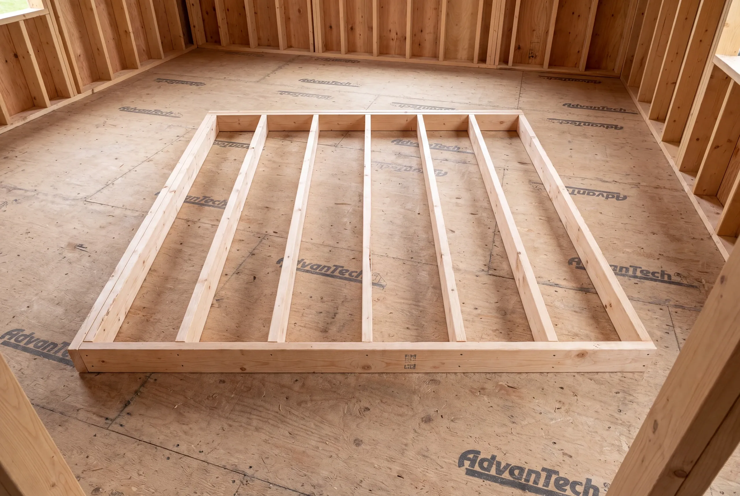 A wooden wall frame lies flat on a subfloor inside a room under construction.