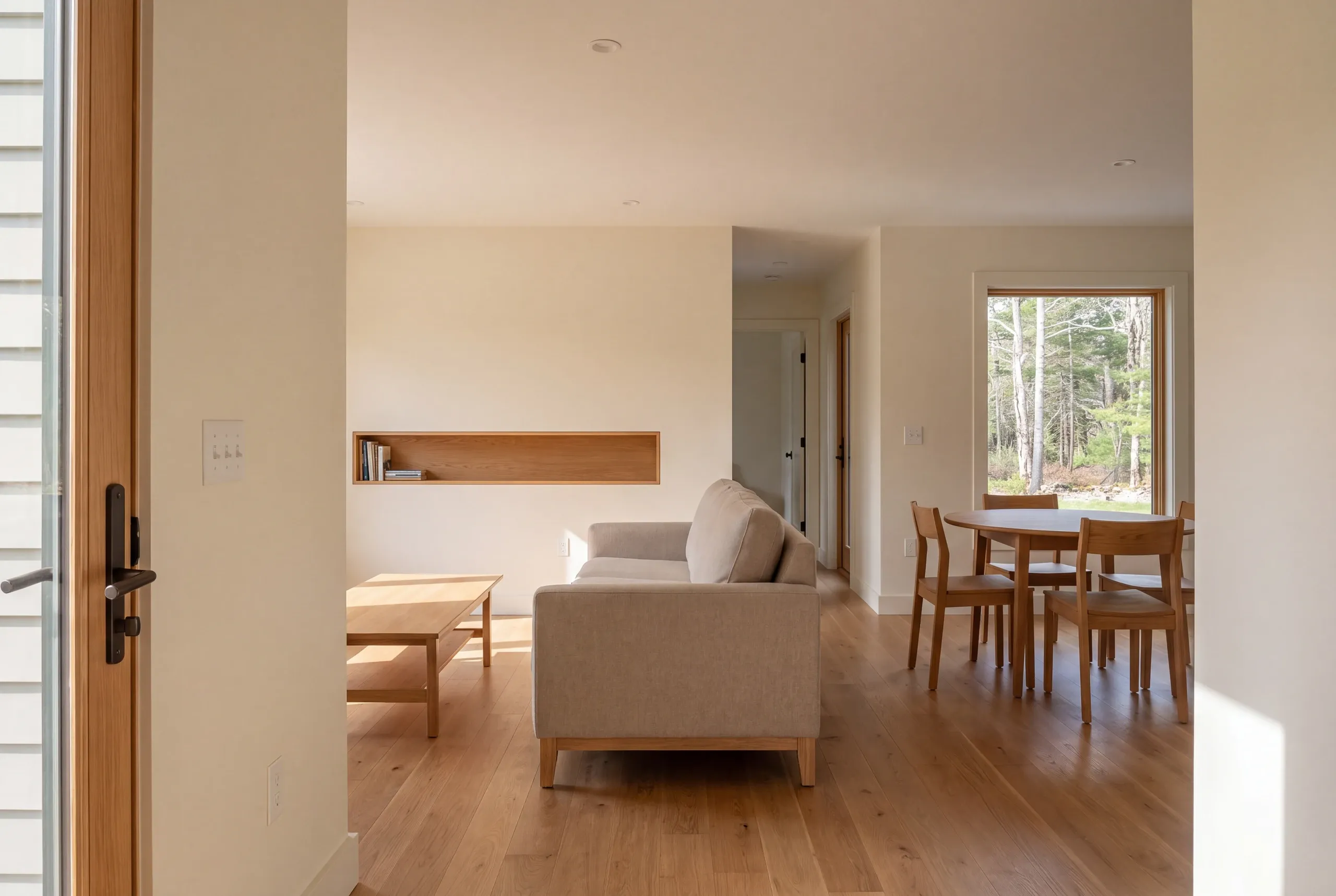 An interior view looking from an entryway into a connected living room and dining area with wooden flooring and furniture.