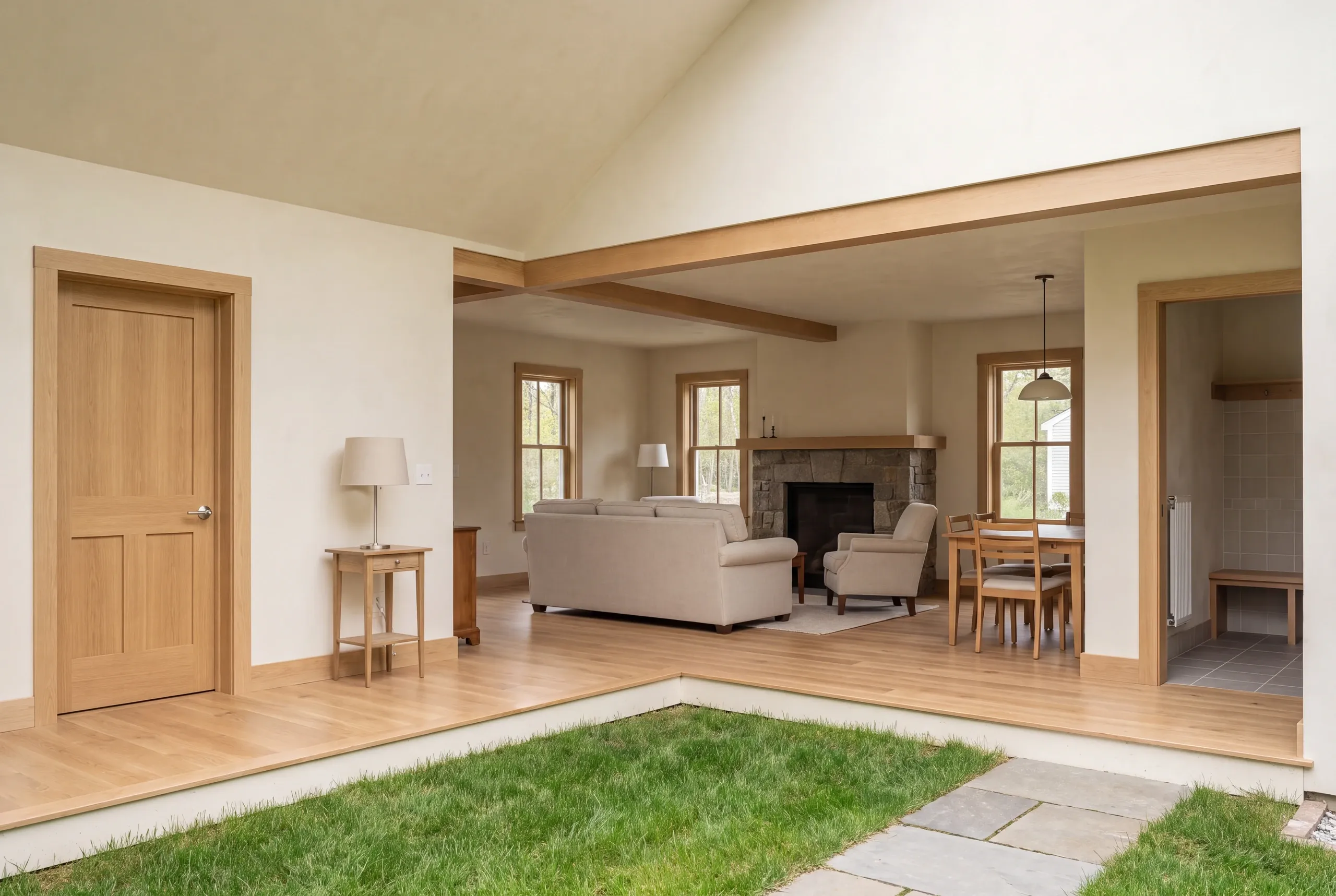 An interior view featuring a sunken grass courtyard opening up to a connected living room and dining space with wooden floors, a stone fireplace, and light-colored walls.
