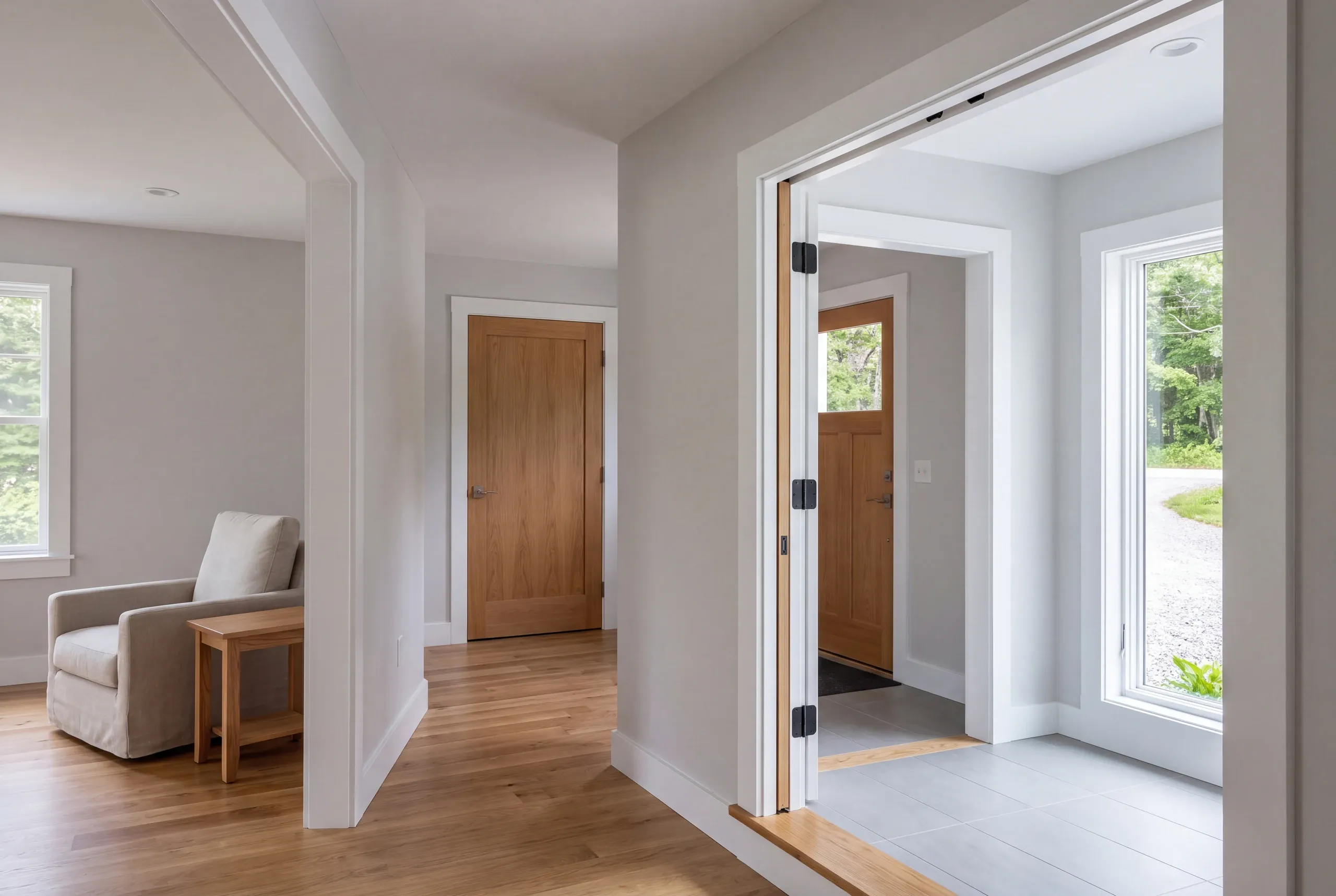 An interior view showing a finished entryway with light grey walls, white trim, hardwood floors, and a tiled foyer.