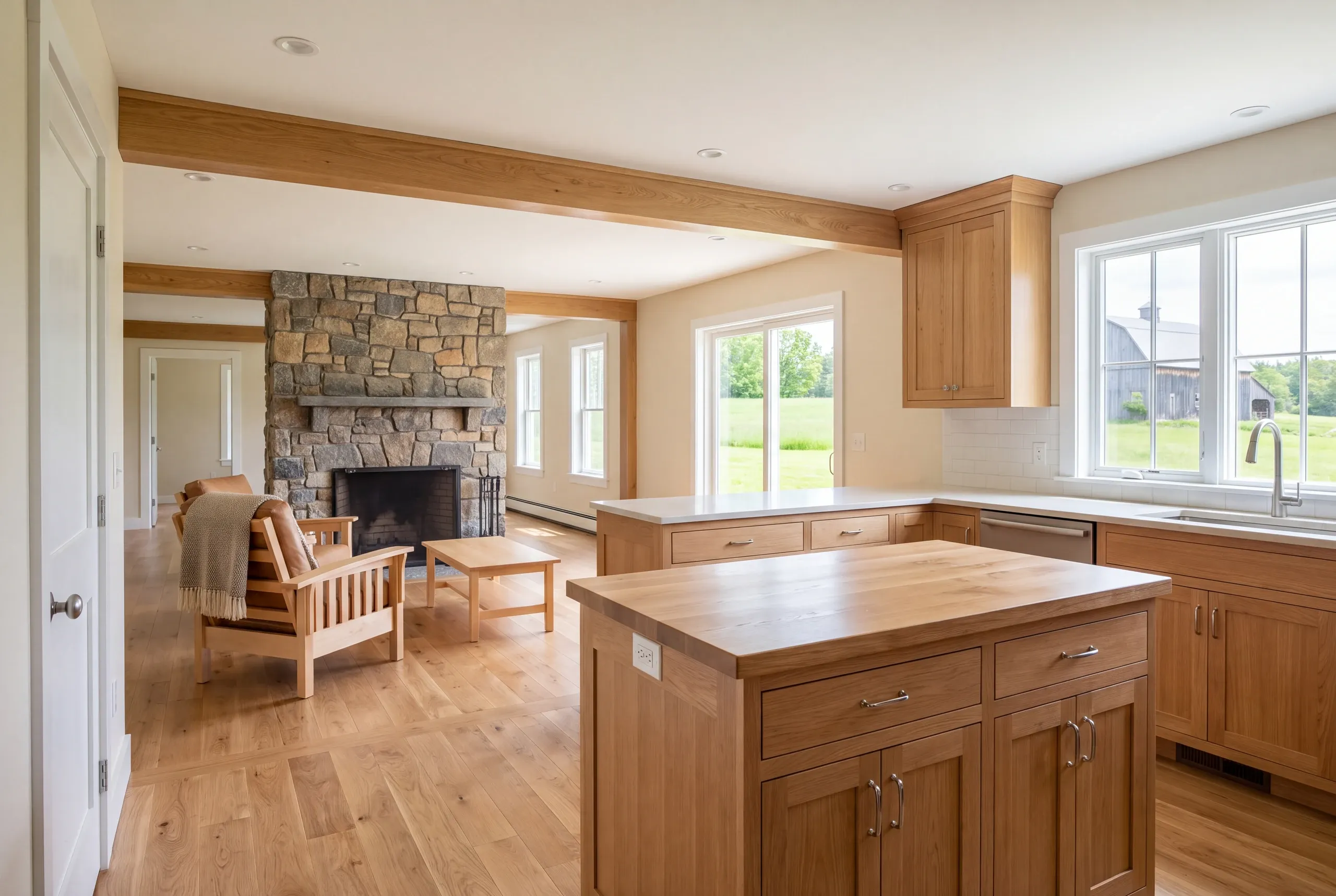 A newly remodeled kitchen with wooden cabinets and island opens directly into a finished living room featuring a stone fireplace and armchairs.