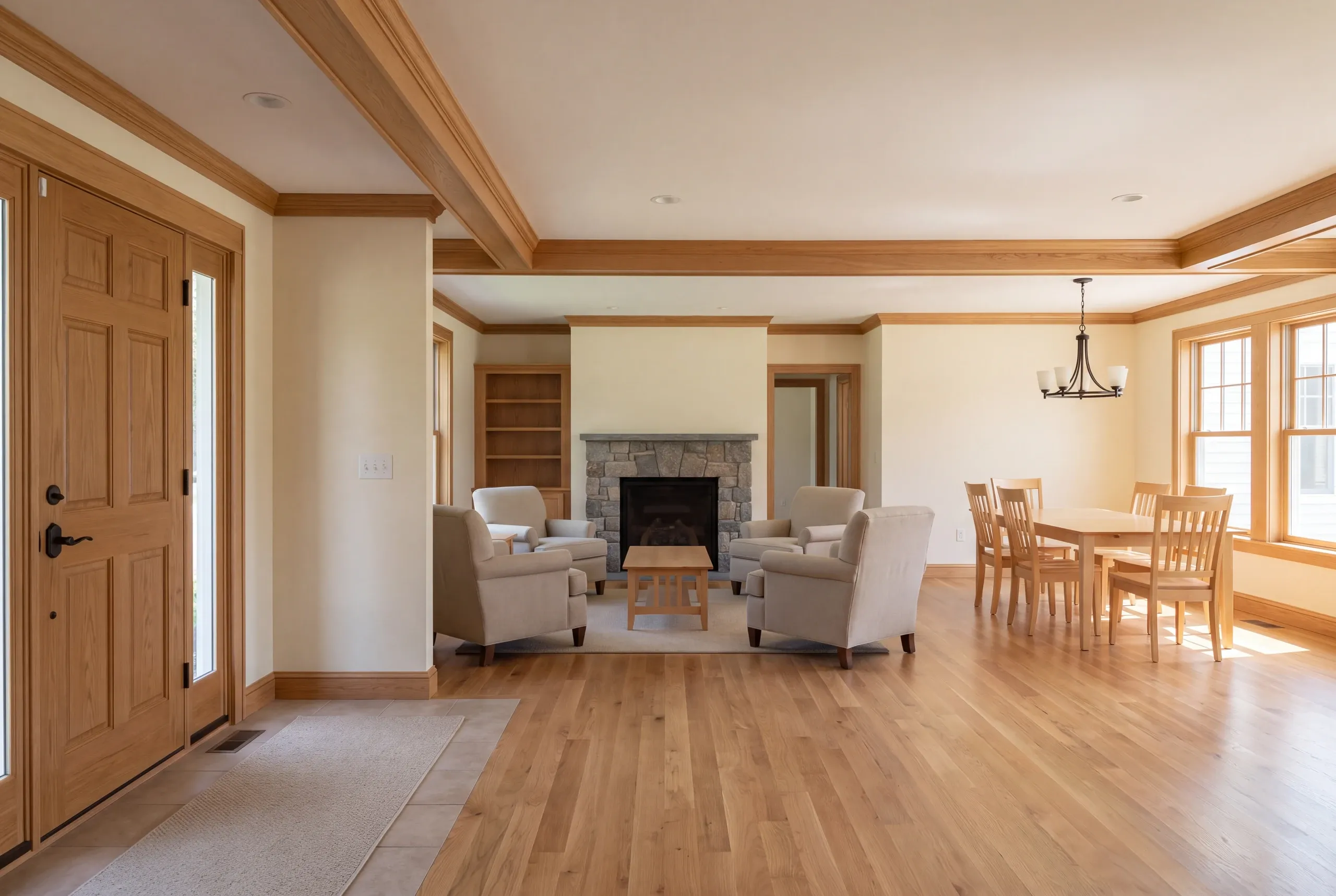 Interior view showing a connected entryway, living room area with a stone fireplace, and a dining space with wooden furniture.