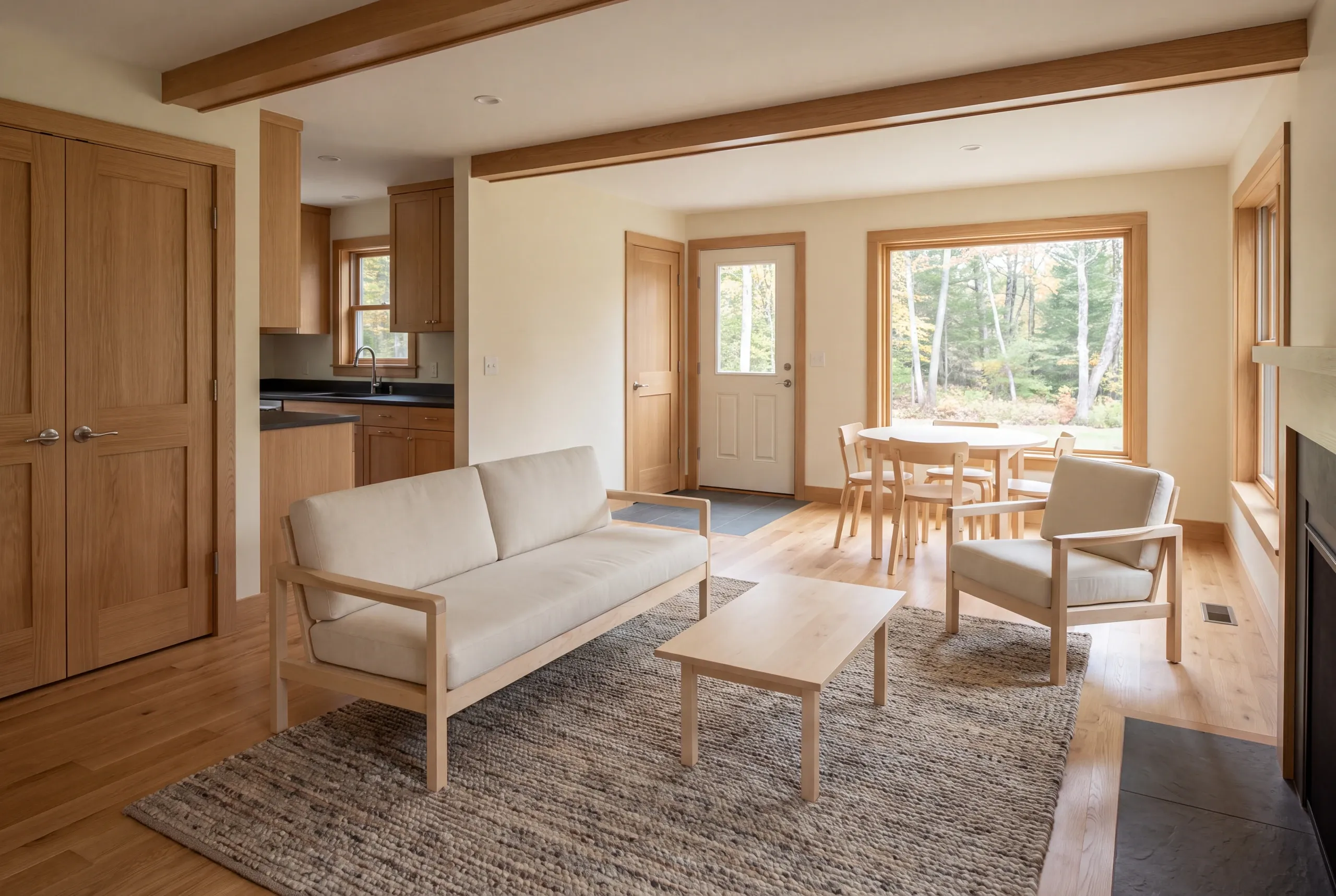 Interior view of a finished living room and dining area featuring a light-colored sofa, armchair, coffee table, and a dining set near a large window.