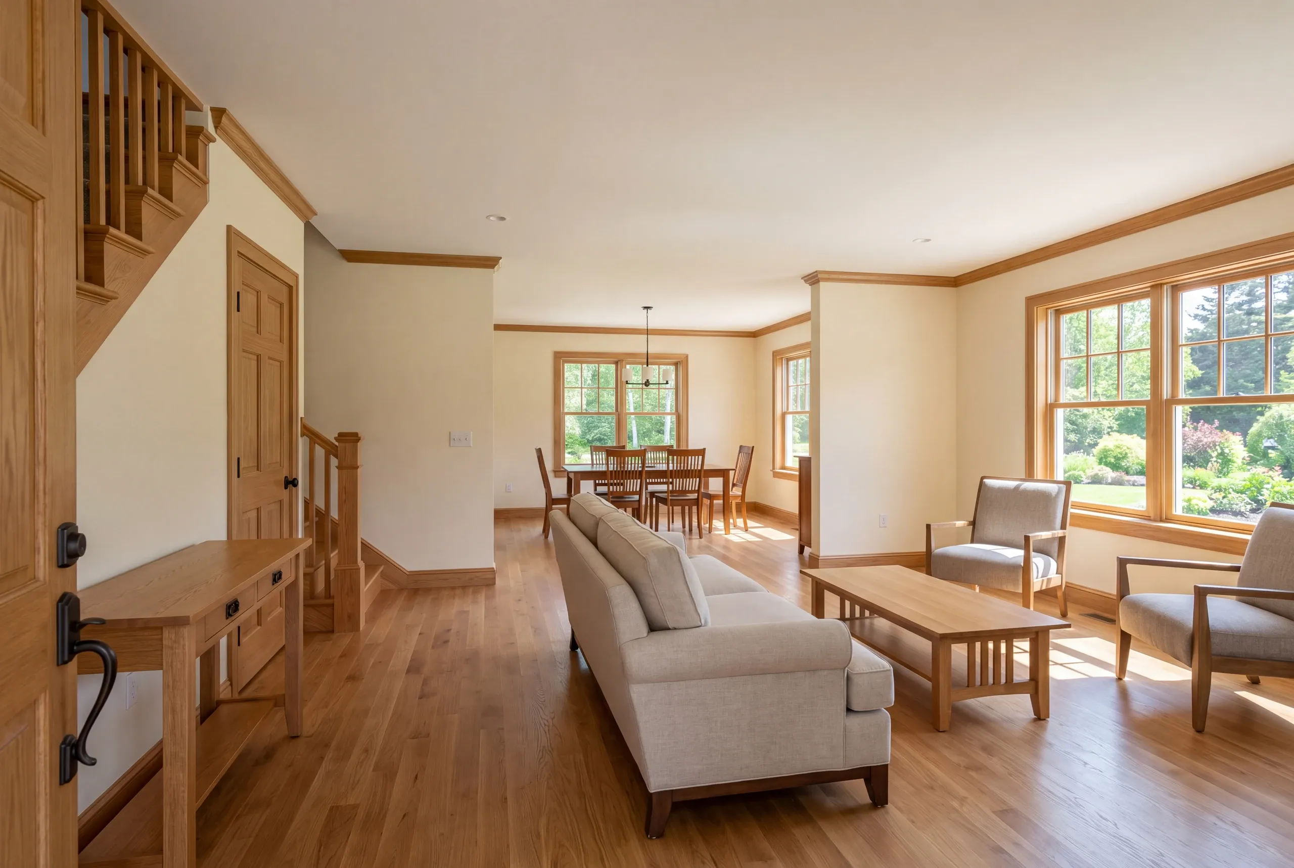 A finished interior view showing a connected entryway, living room with a sofa and armchairs, and a dining area in the background.
