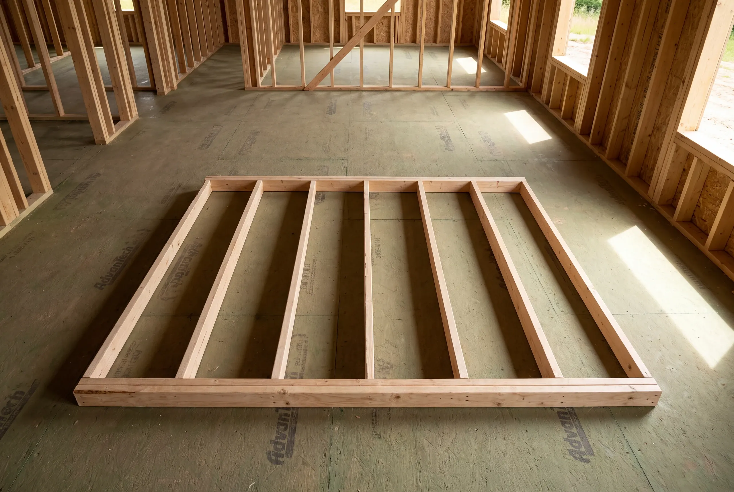A single wooden wall frame lies flat on a subfloor inside a home under construction.