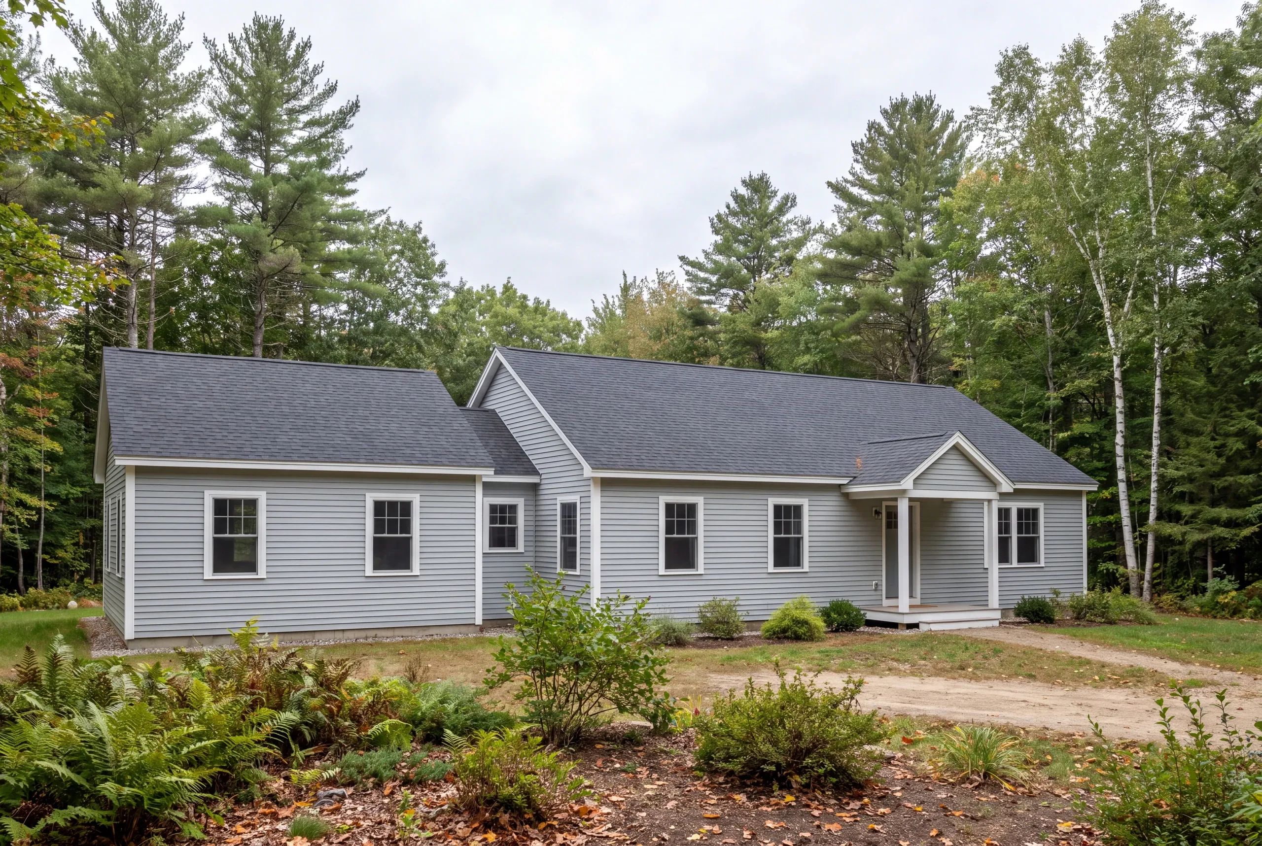 Exterior view of a single-story gray-sided house with a dark shingle roof, surrounded by trees and vegetation.