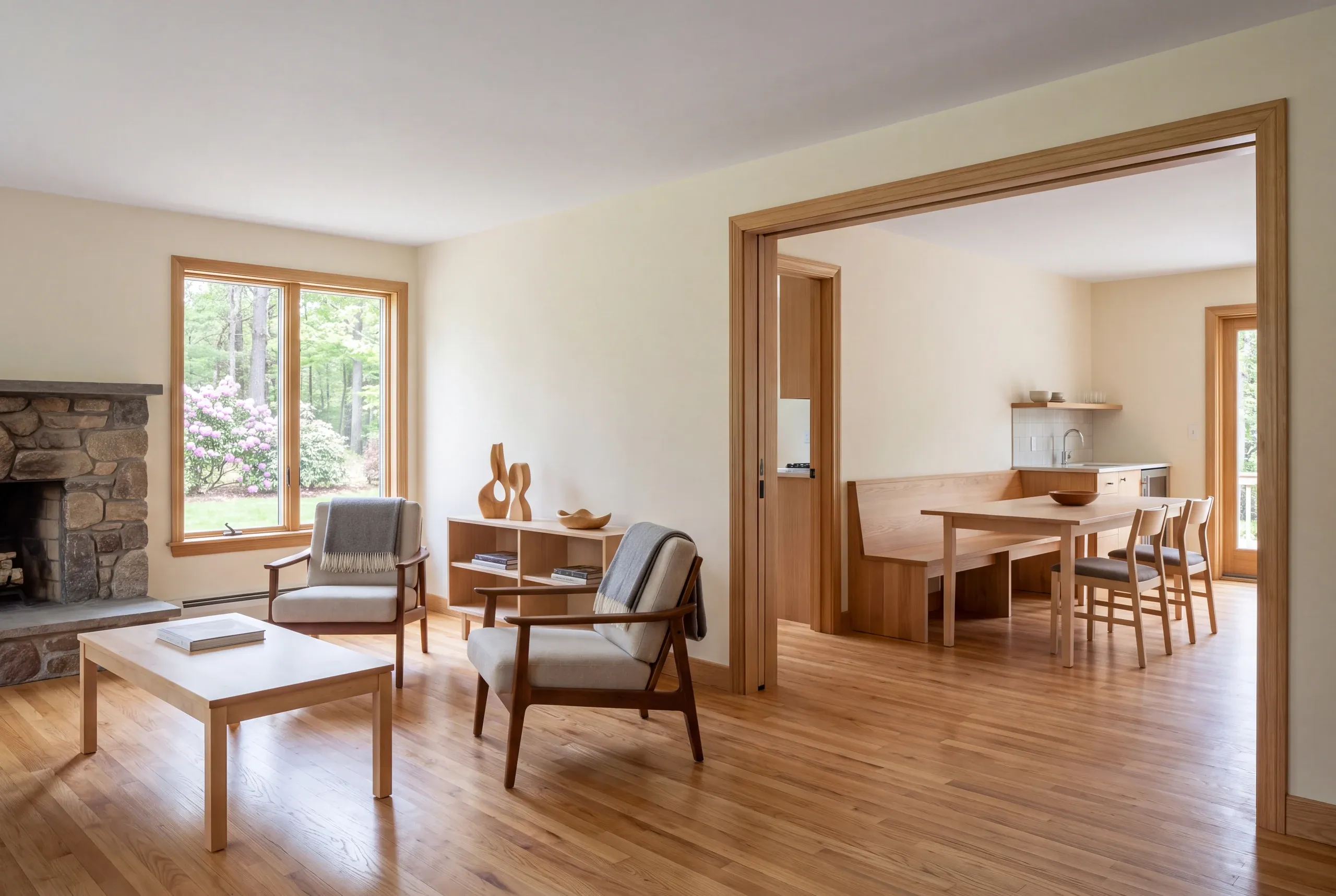 A bright finished living room with hardwood floors, a stone fireplace, and a wide wooden cased opening connecting to an adjacent dining area.
