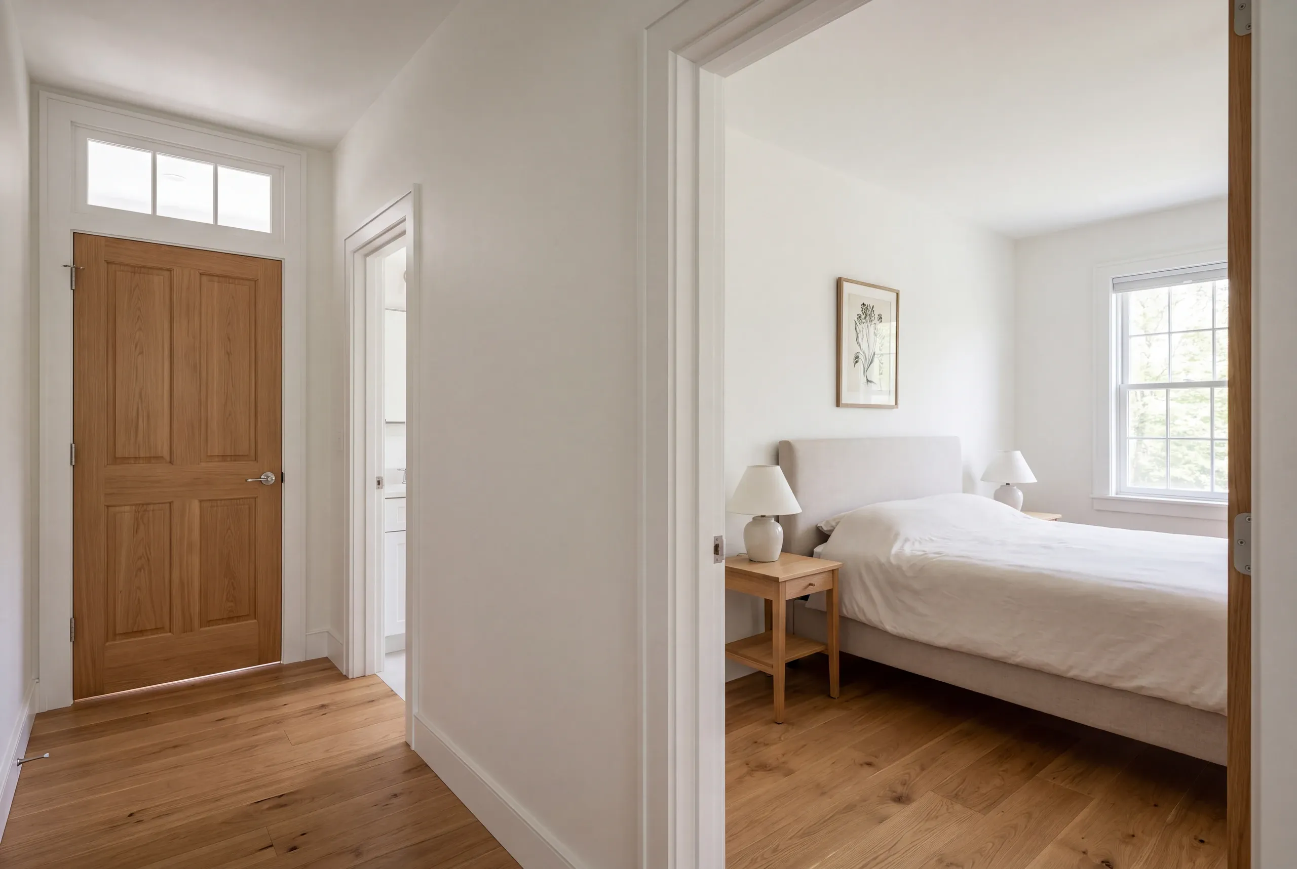 Interior hallway with a wooden door, hardwood floors, and an open doorway revealing a furnished bedroom suite.