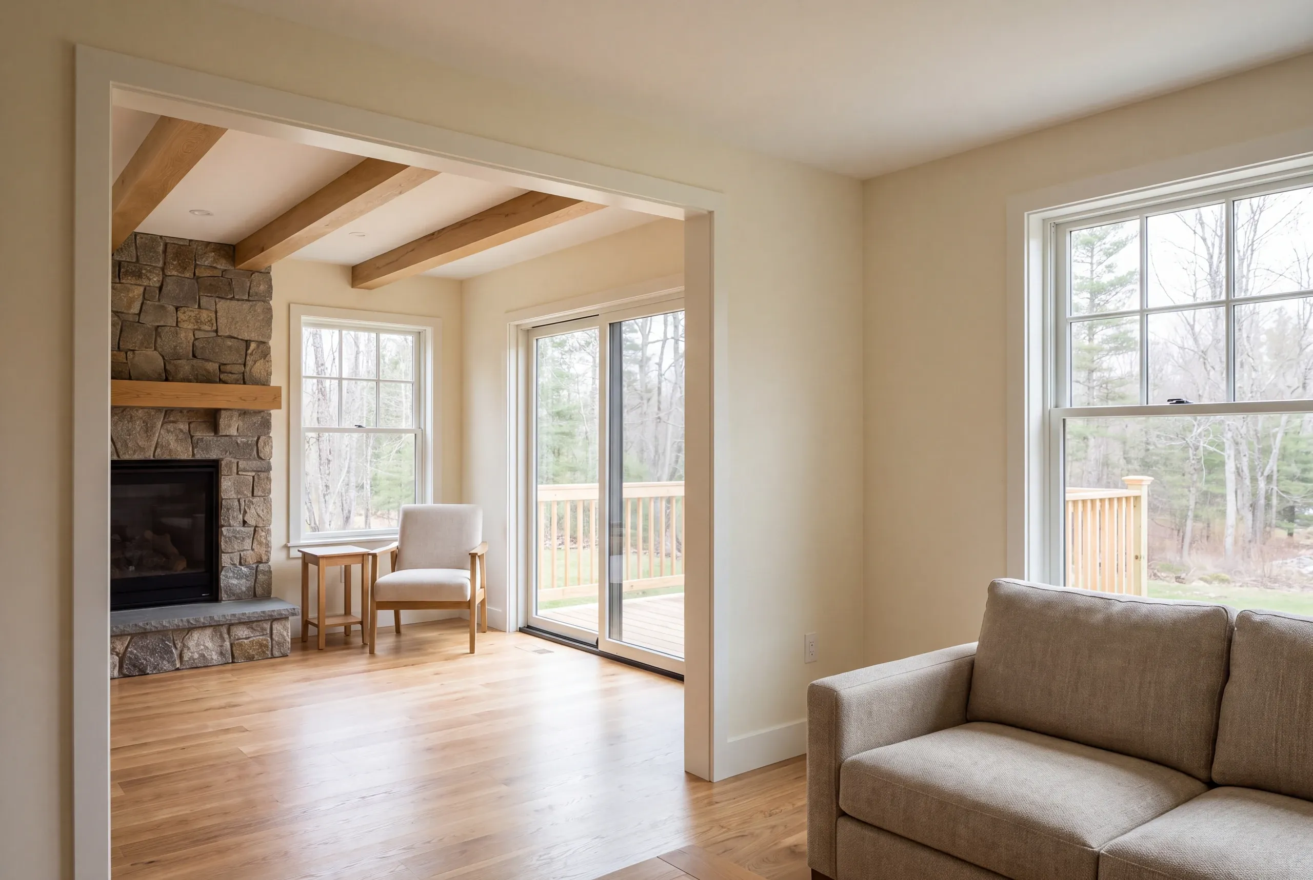 Interior view showing a finished room with a stone fireplace and hardwood floors opening through a wide doorway into an adjacent carpeted living area.