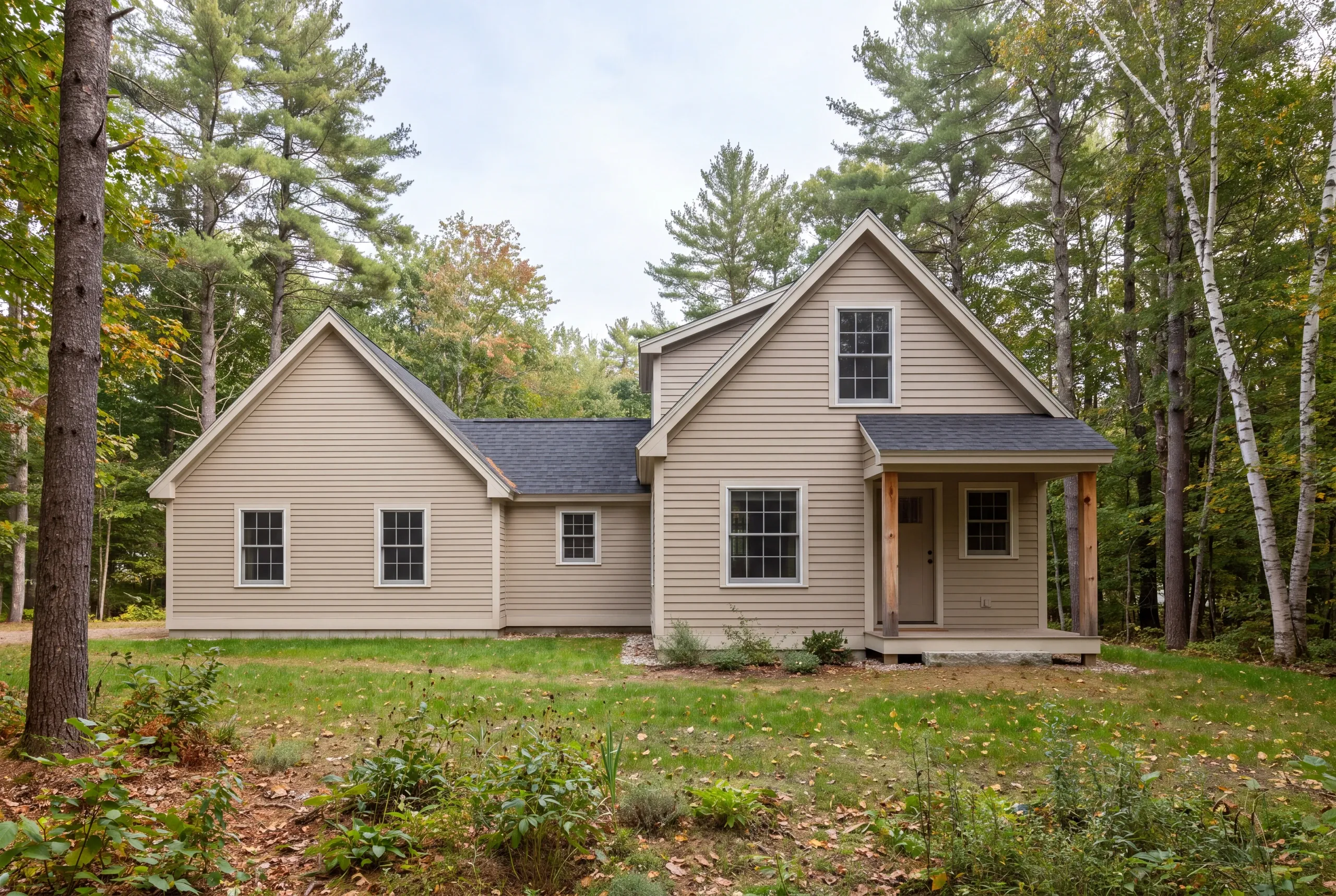 A two-story tan-sided house with a matching attached wing surrounded by trees.