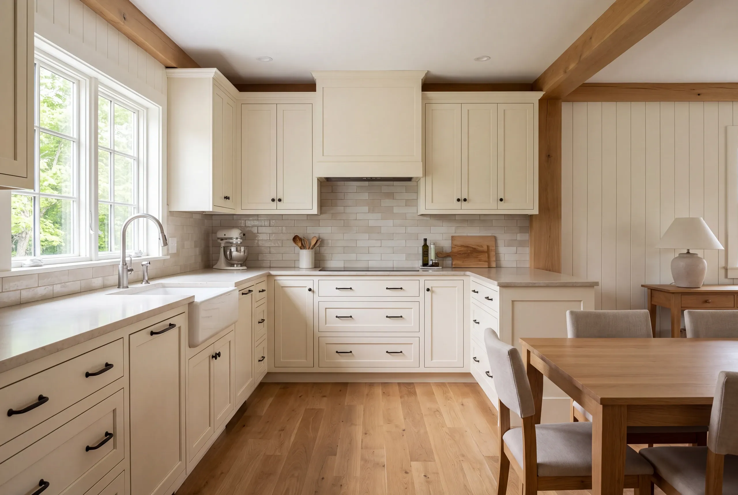 A bright kitchen features off-white shaker cabinets, pale countertops, light tile backsplash, and wooden beams on the ceiling.