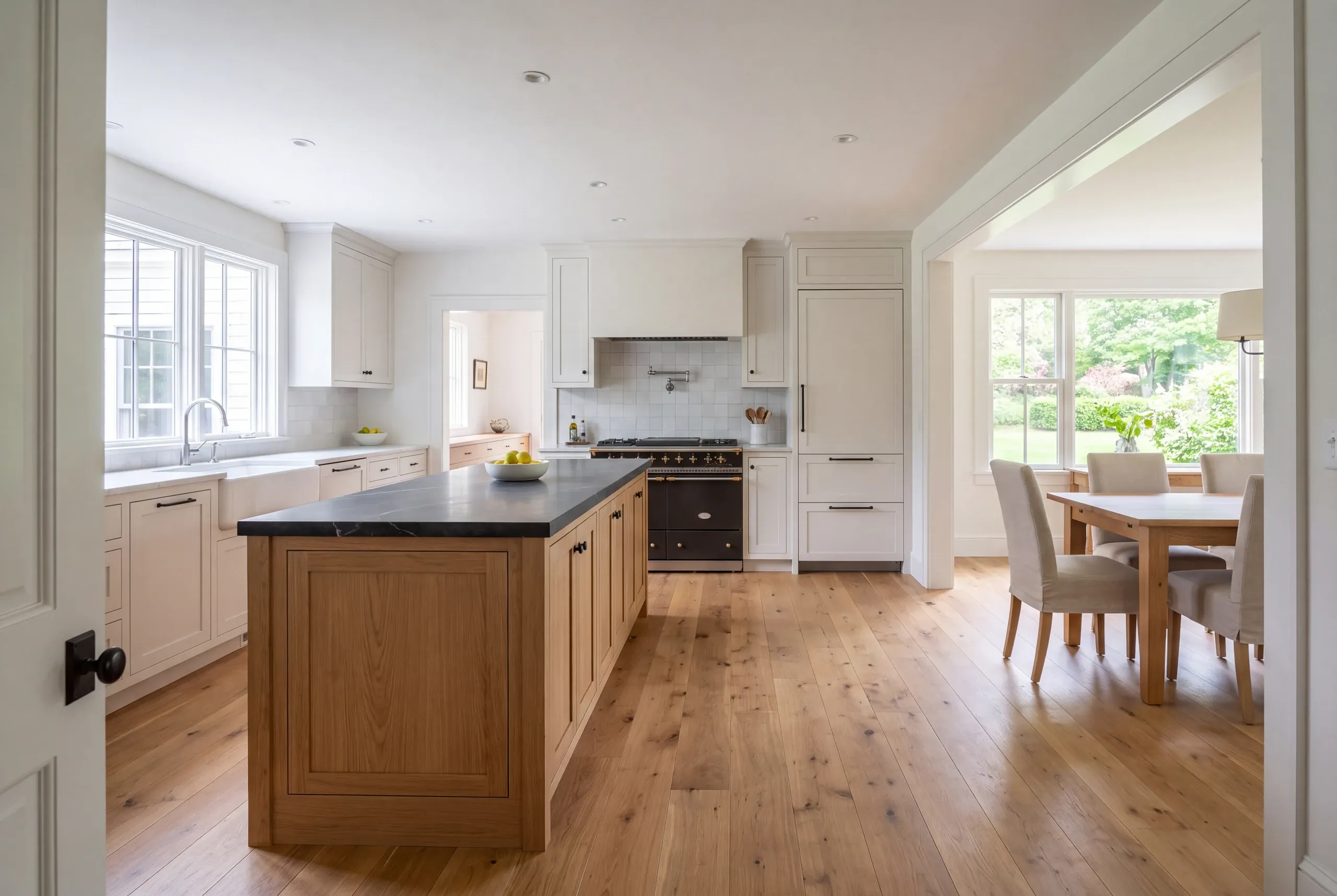A newly finished kitchen featuring a wooden central island, dark countertops, white cabinetry, hardwood floors, and an adjacent dining space.