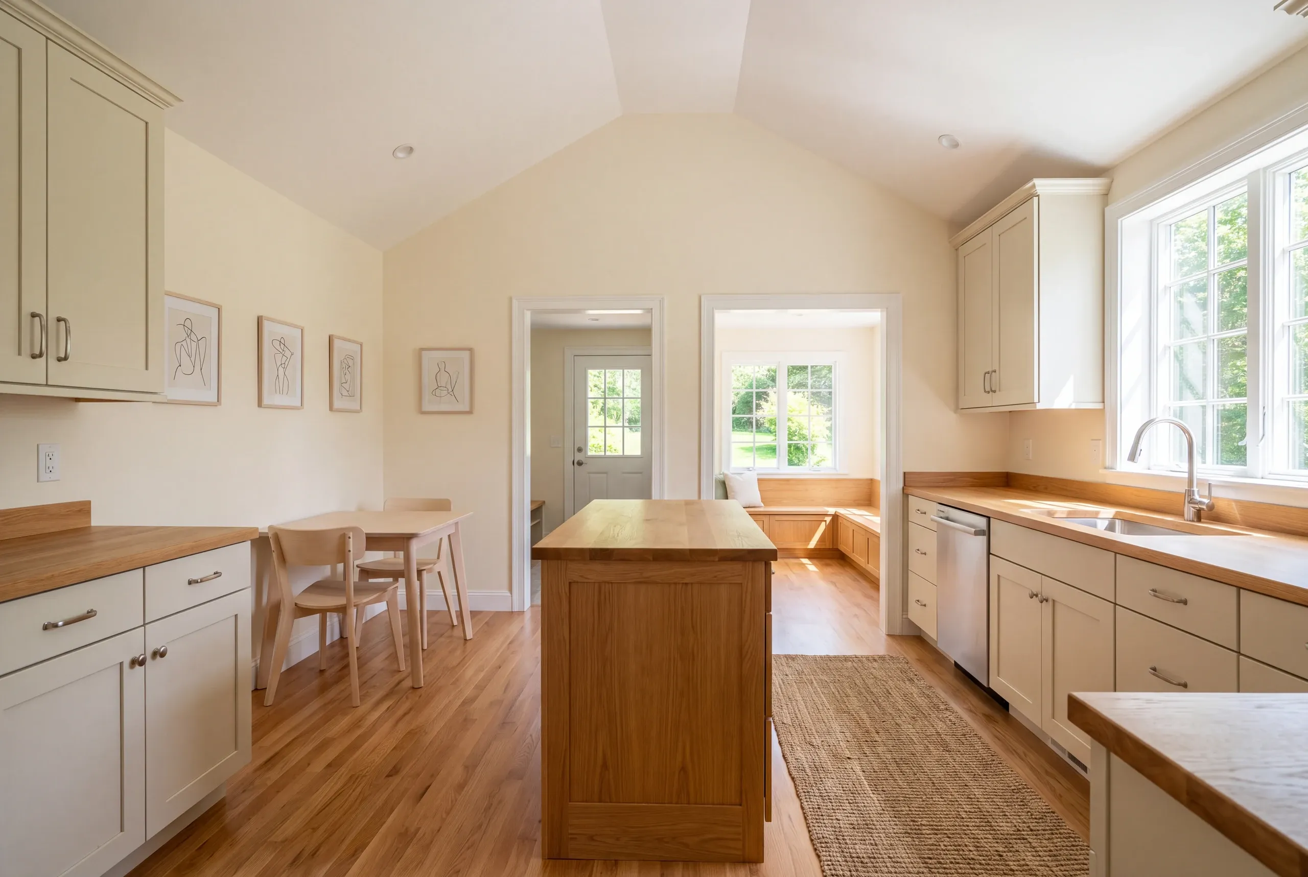 A finished kitchen with light cream shaker cabinets, wood countertops, an island, and a dining table.