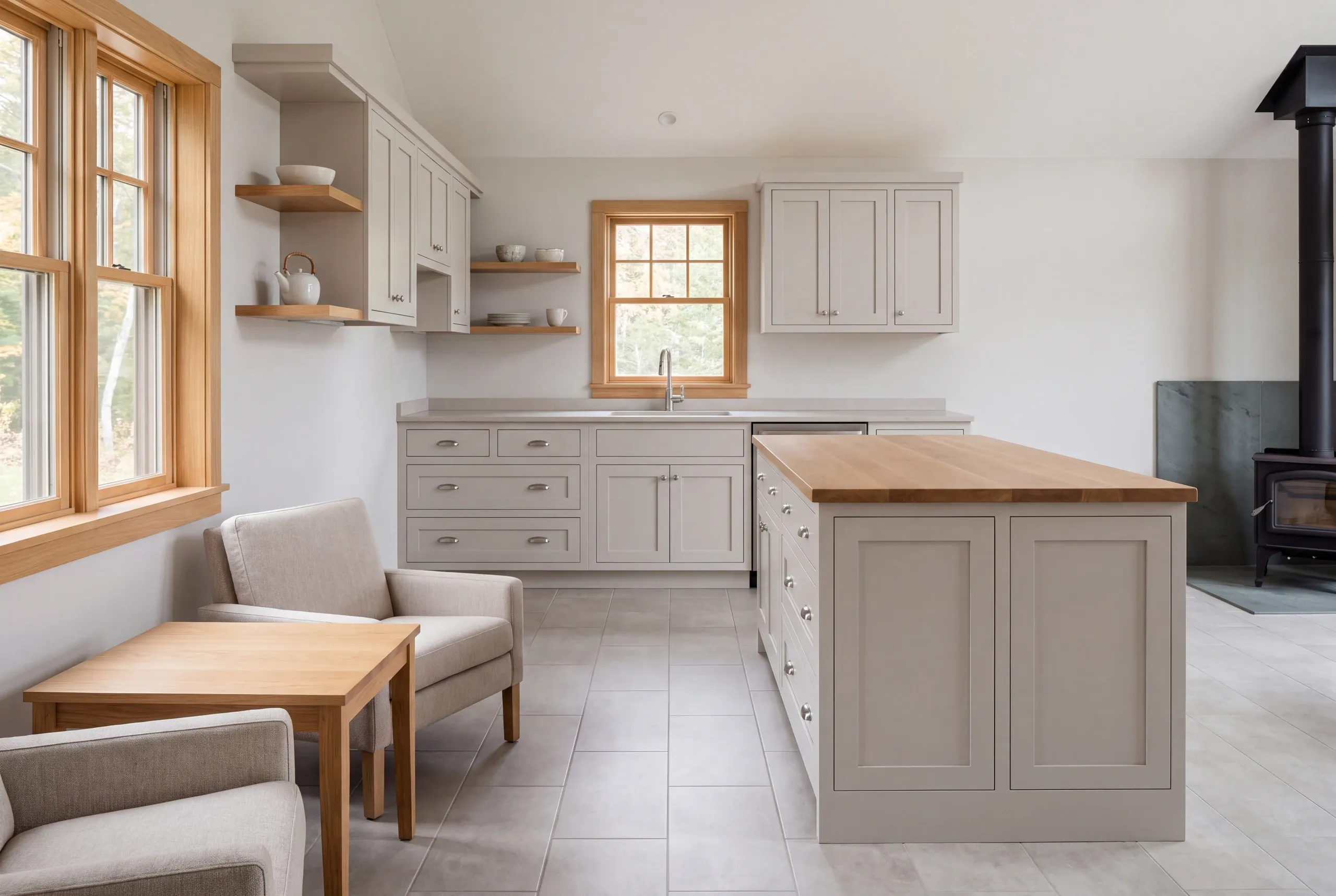 A bright kitchen interior features light gray shaker cabinets, a central island with a wood countertop, and tile flooring.