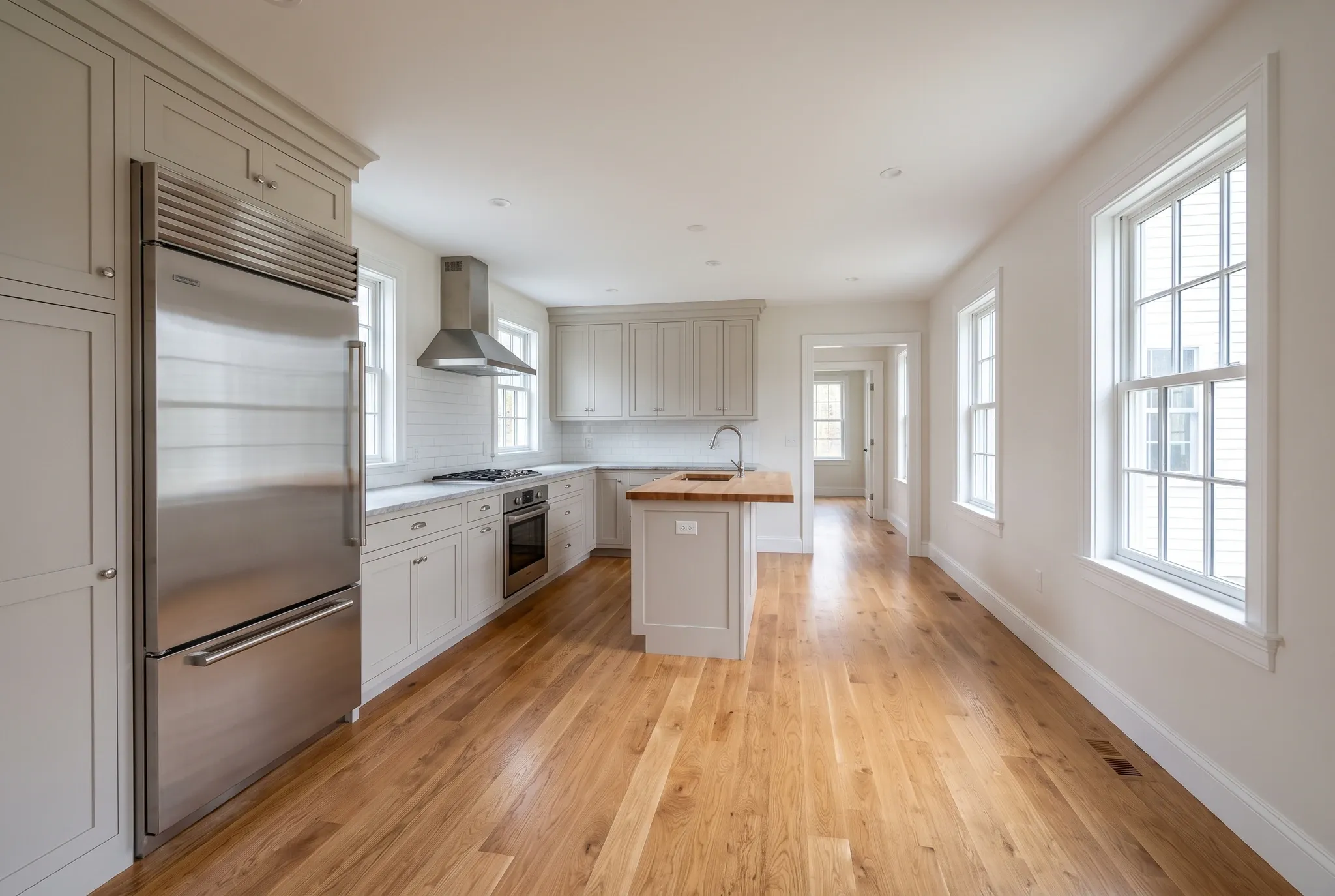 A finished kitchen featuring light grey cabinetry, hardwood floors, a stainless steel refrigerator, and a small center island.