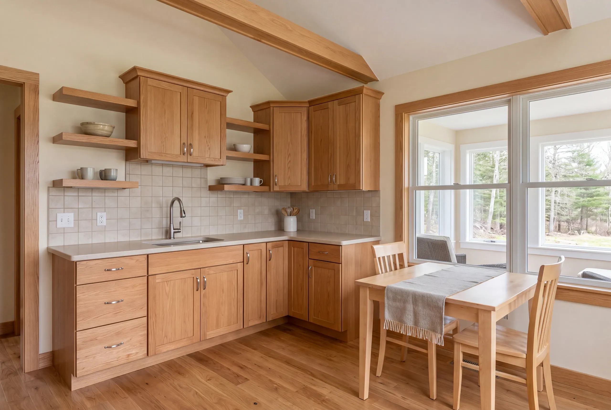 A finished kitchen featuring wooden cabinetry, tiled backsplash, countertops, sink, and an adjacent small dining table with chairs.