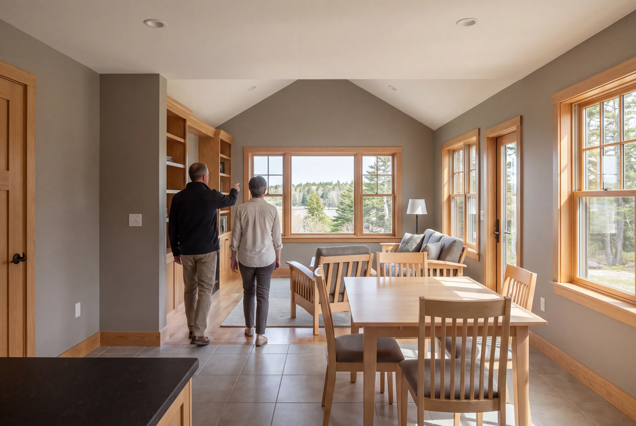 Two adults seen from behind walking through a finished living and dining area with wood trim.