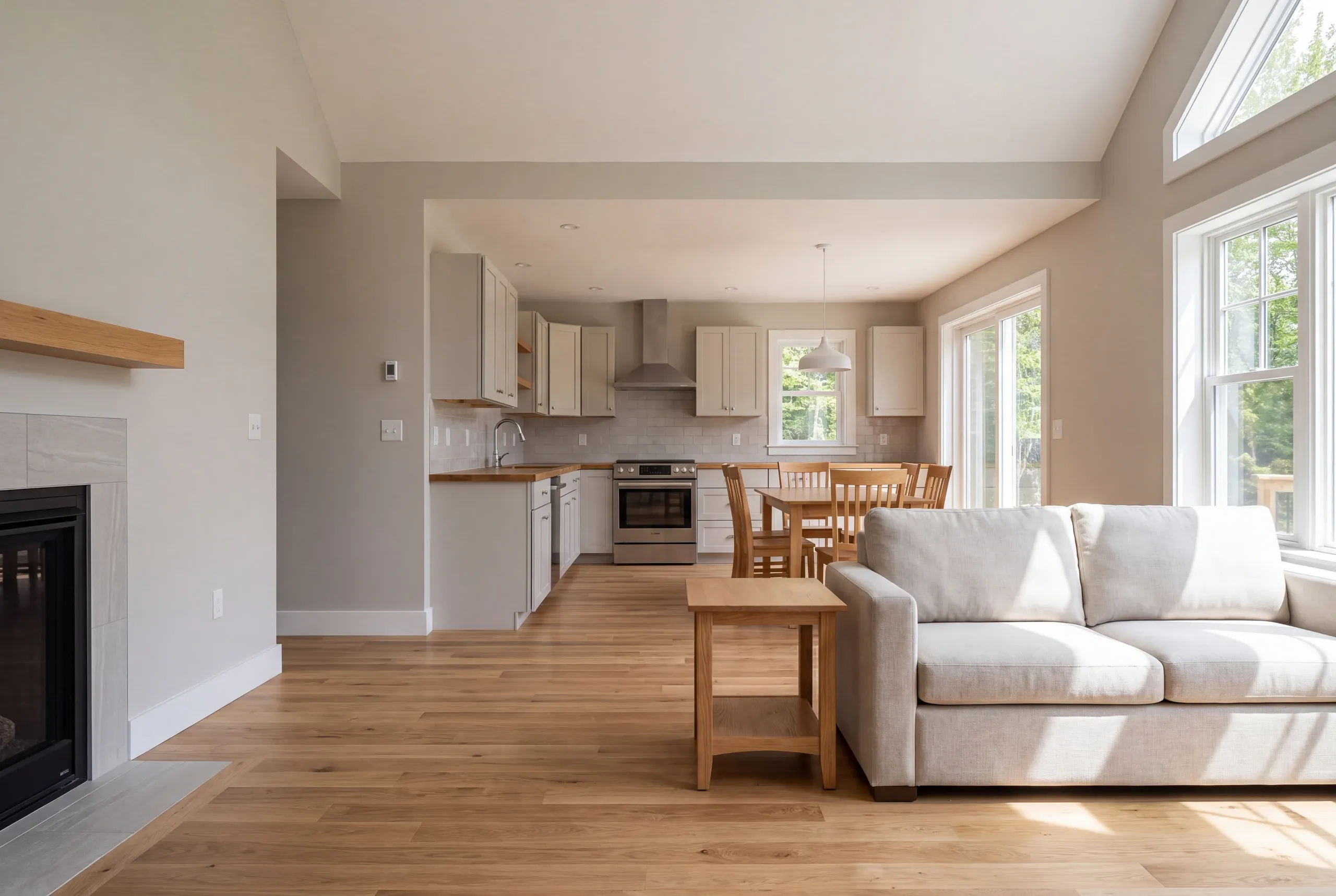 Interior view showing a connected living area with a fireplace, a kitchen in the background, and a dining table set further back.